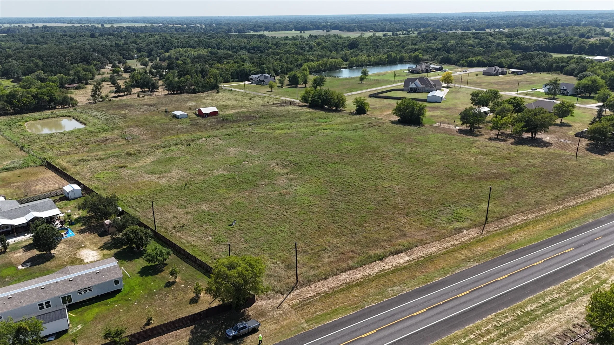 Expansive open land featuring a clear pond, mature trees, and a red barn structure