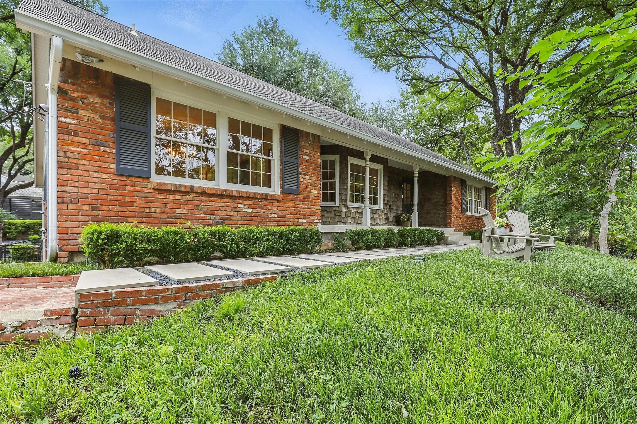 Single story home featuring brick siding, covered porch, a front lawn, and roof with shingles