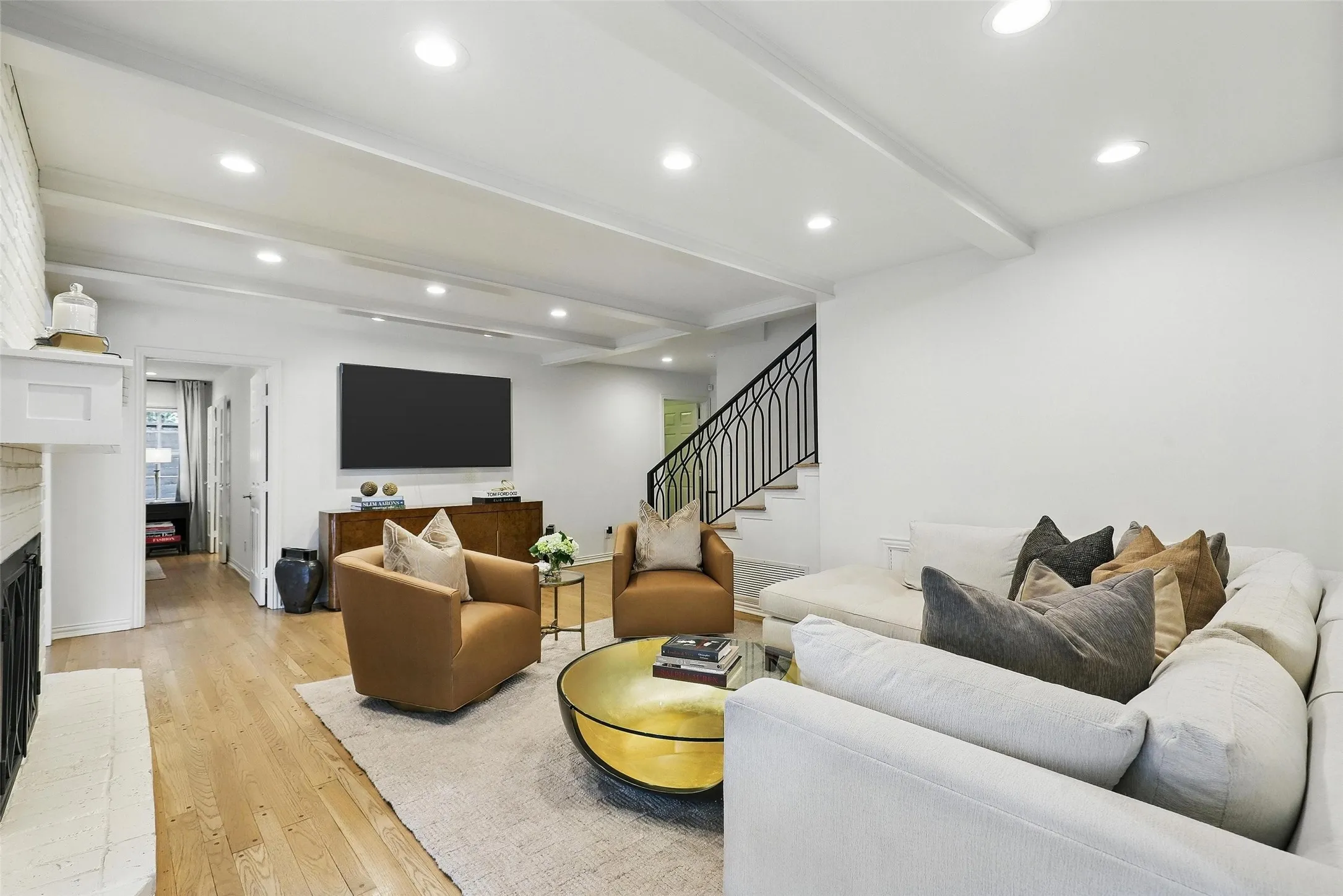 Living room with a brick fireplace, beam ceiling, light wood finished floors, recessed lighting, and stairs
