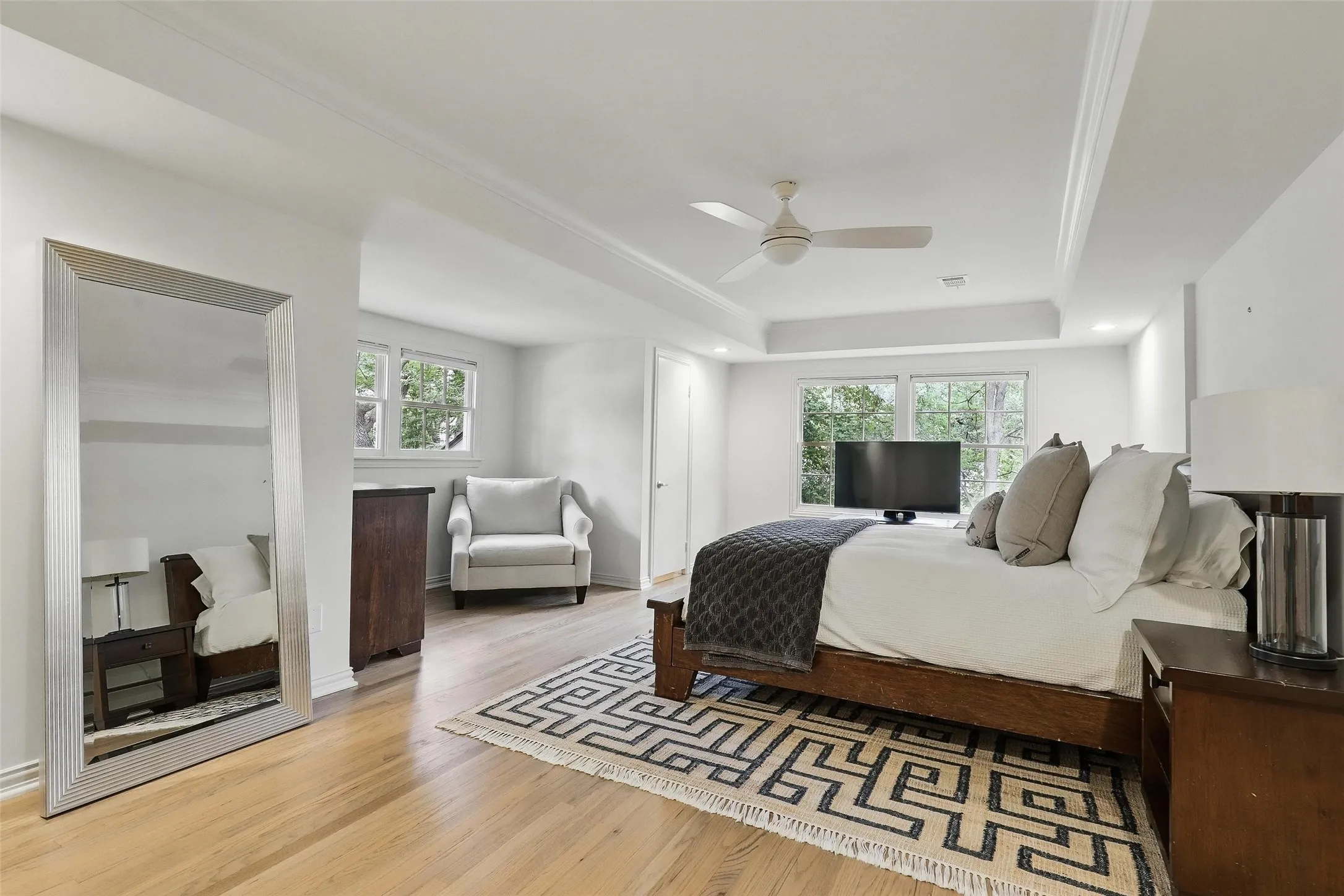 Bedroom with multiple windows, light wood-type flooring, a ceiling fan, and a raised ceiling
