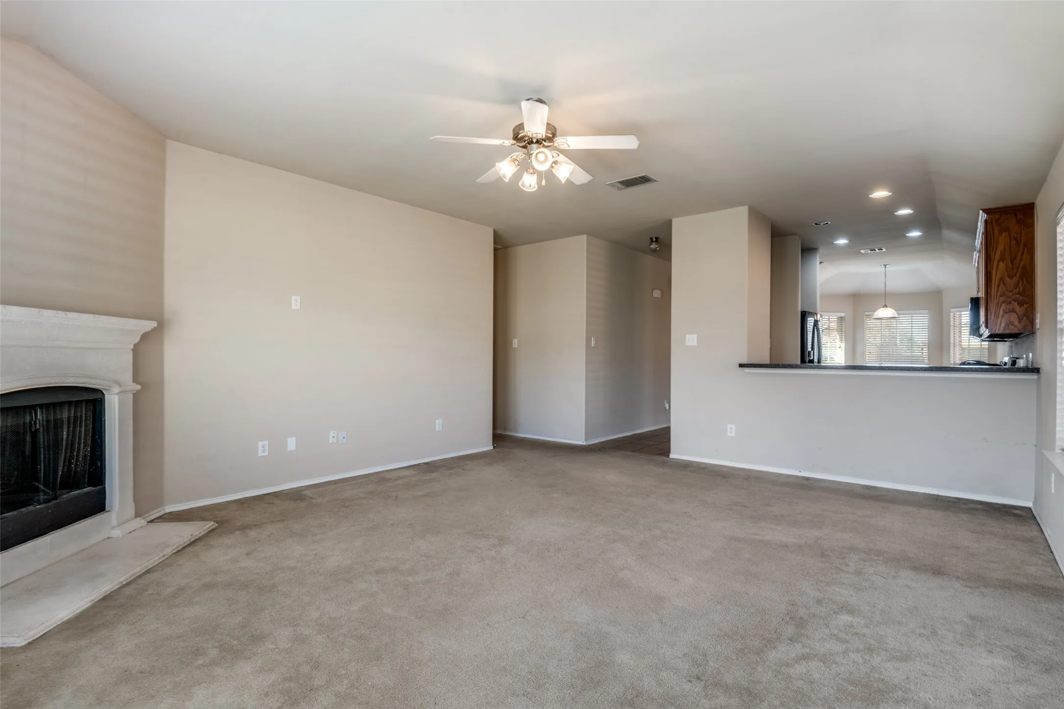 Spacious living area featuring a fireplace with a stone surround, a ceiling fan, and carpet flooring