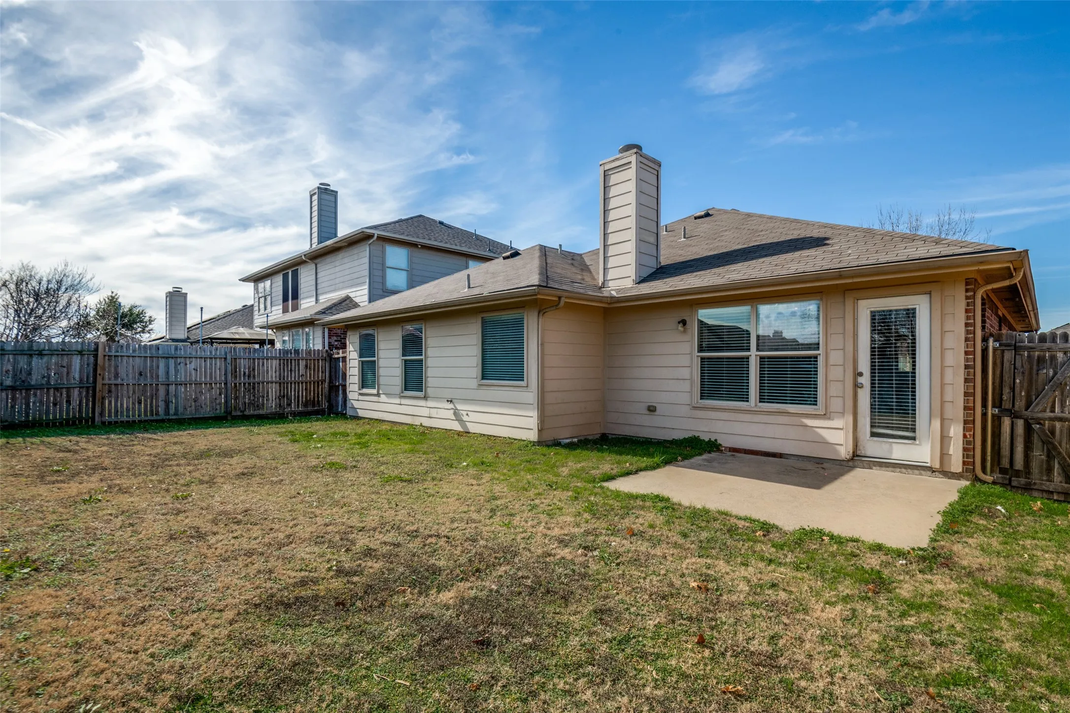 Expansive backyard featuring a concrete patio, a full privacy fence, and a rear door with an integrated window