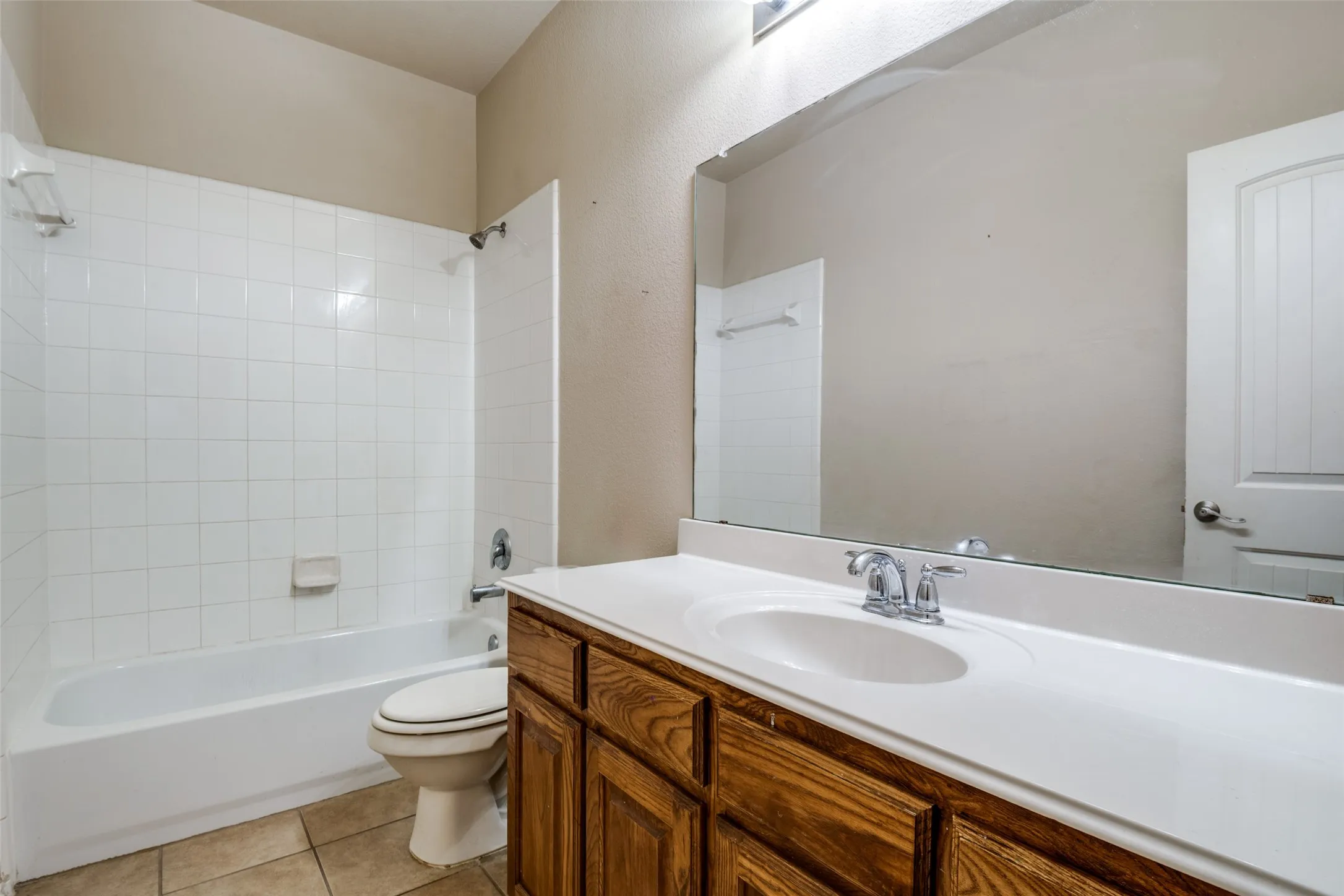 Bathroom featuring a white bathtub, ceramic tile shower surround, wood-finish vanity with a white countertop, oval undermount sink, and a large wall-mounted mirror