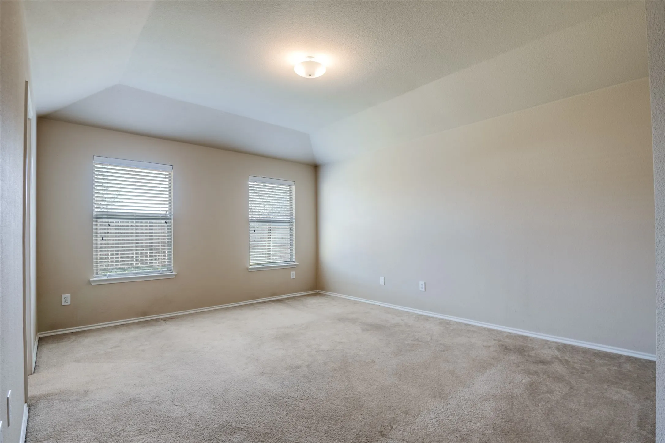 Carpeted room with a tray ceiling and two windows featuring blinds