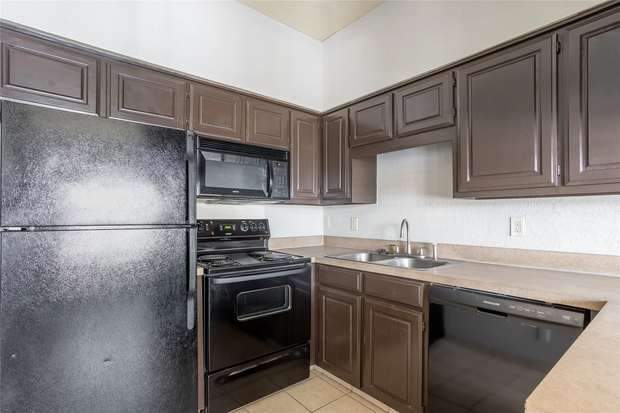 Kitchen with black appliances, light countertops, dark brown cabinets, and light tile patterned flooring