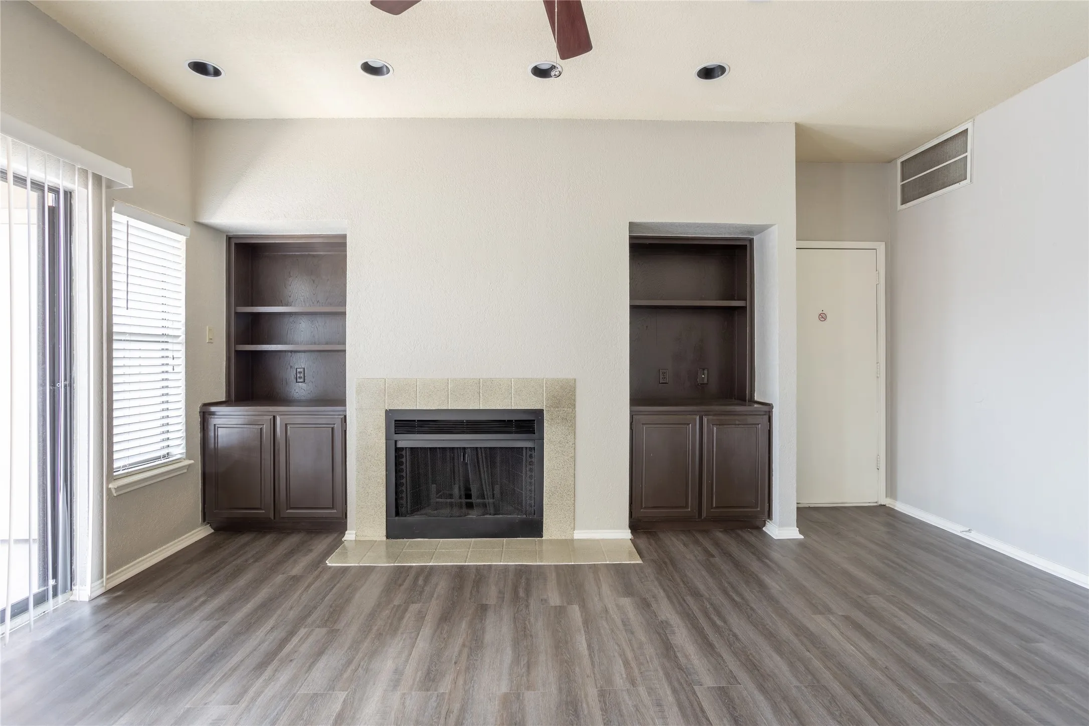 Unfurnished living room with built in shelves, a ceiling fan, dark wood-style flooring, a tiled fireplace, and recessed lighting