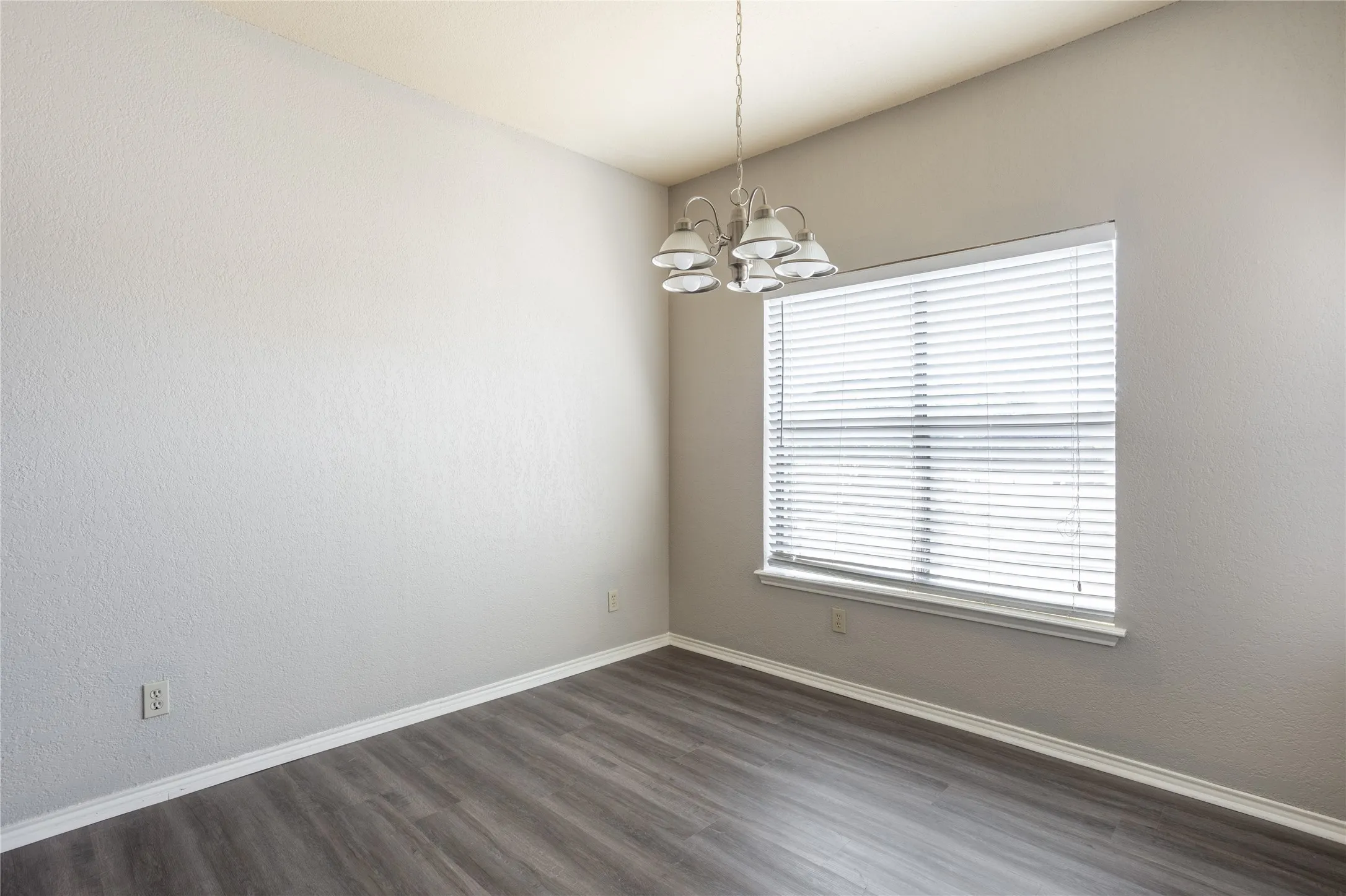 Spare room with dark wood-type flooring, a chandelier, and a textured wall