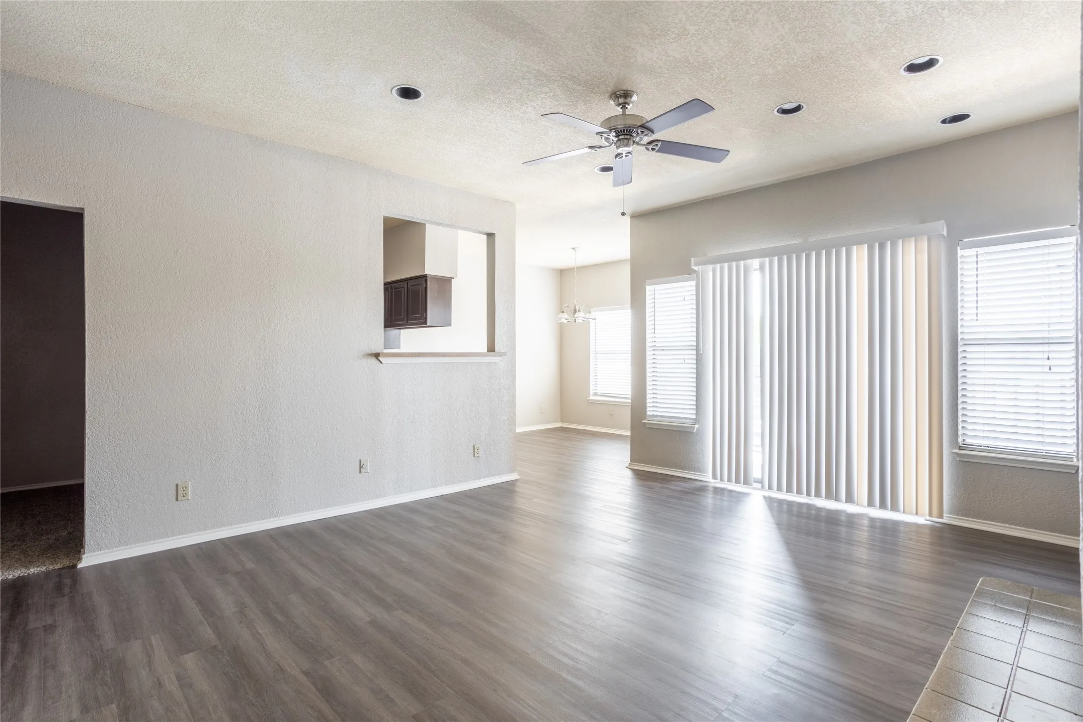 Unfurnished living room featuring dark wood-style floors, a textured ceiling, a ceiling fan, and a chandelier