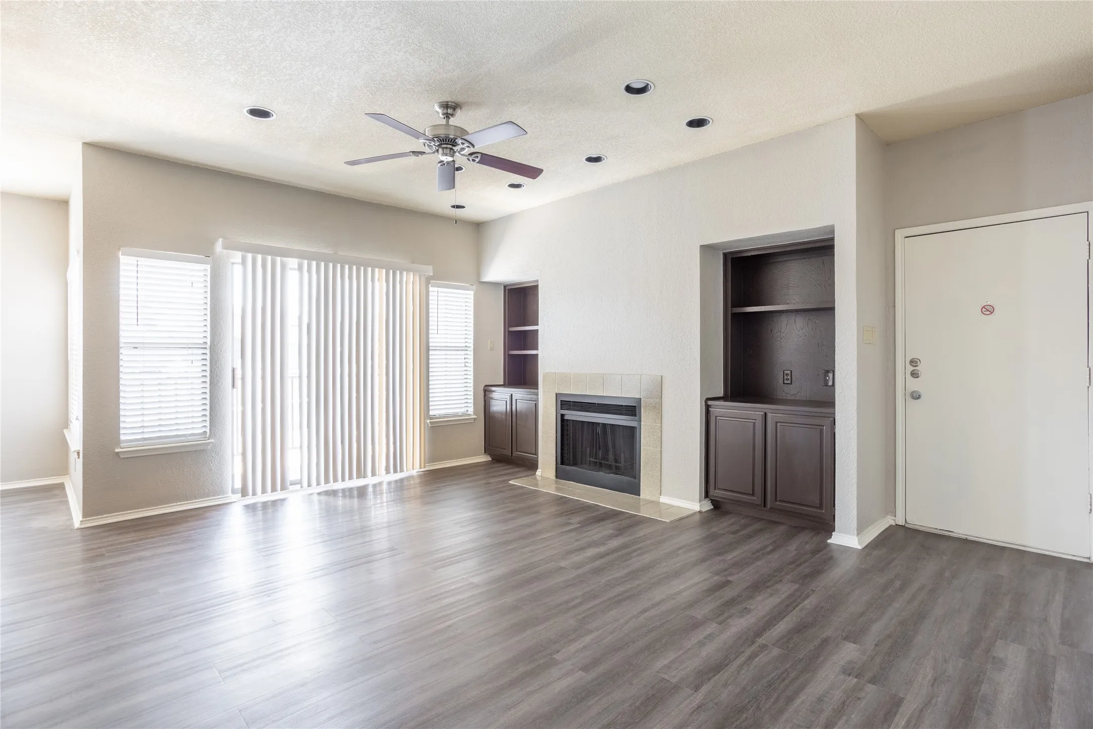 Unfurnished living room featuring a fireplace, a ceiling fan, dark wood finished floors, a textured ceiling, and built in shelves