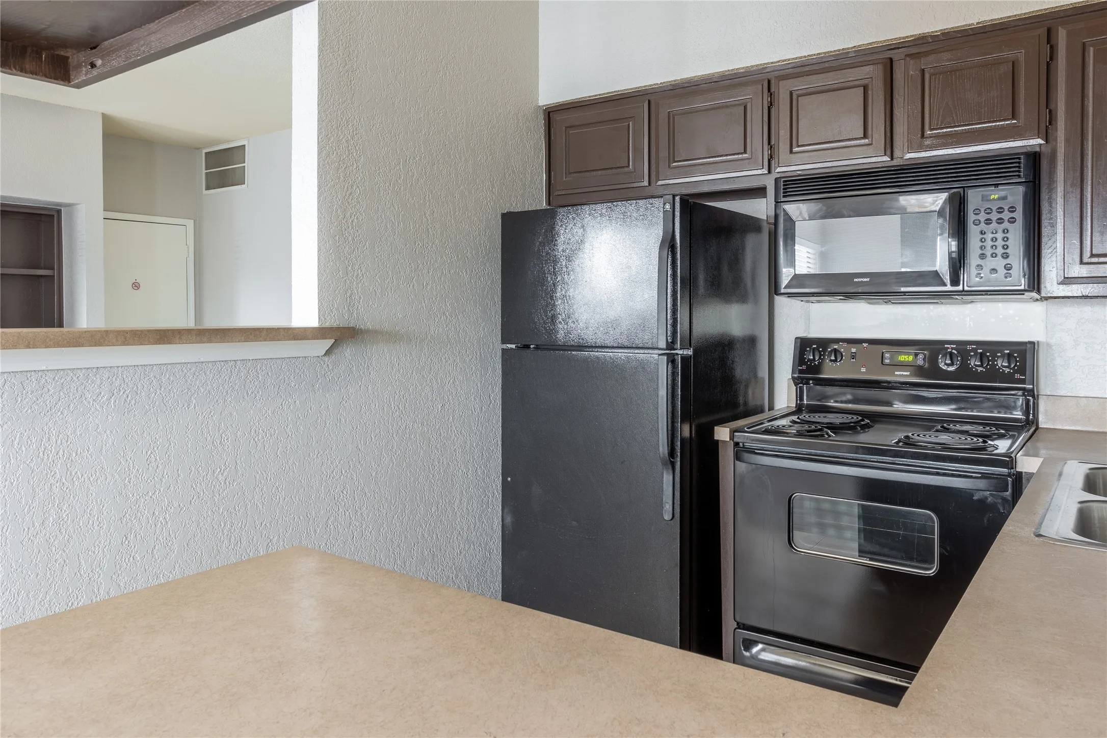 Kitchen featuring black appliances, light countertops, a textured wall, and dark brown cabinets