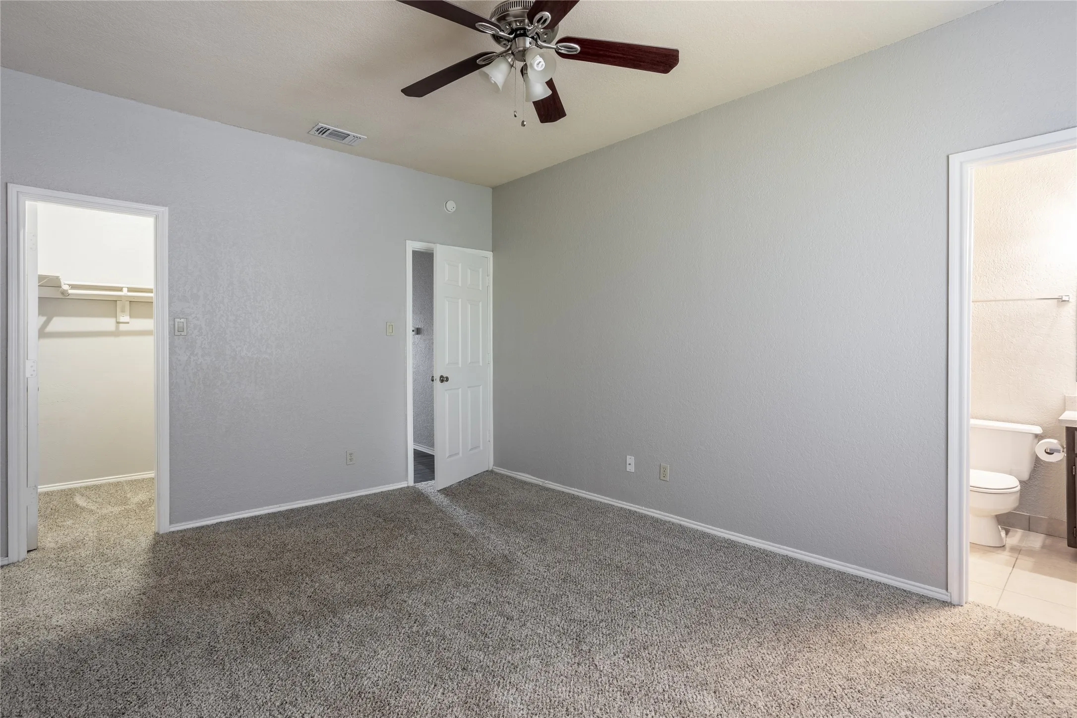 Unfurnished bedroom with light colored carpet, a walk in closet, a ceiling fan, and connected bathroom