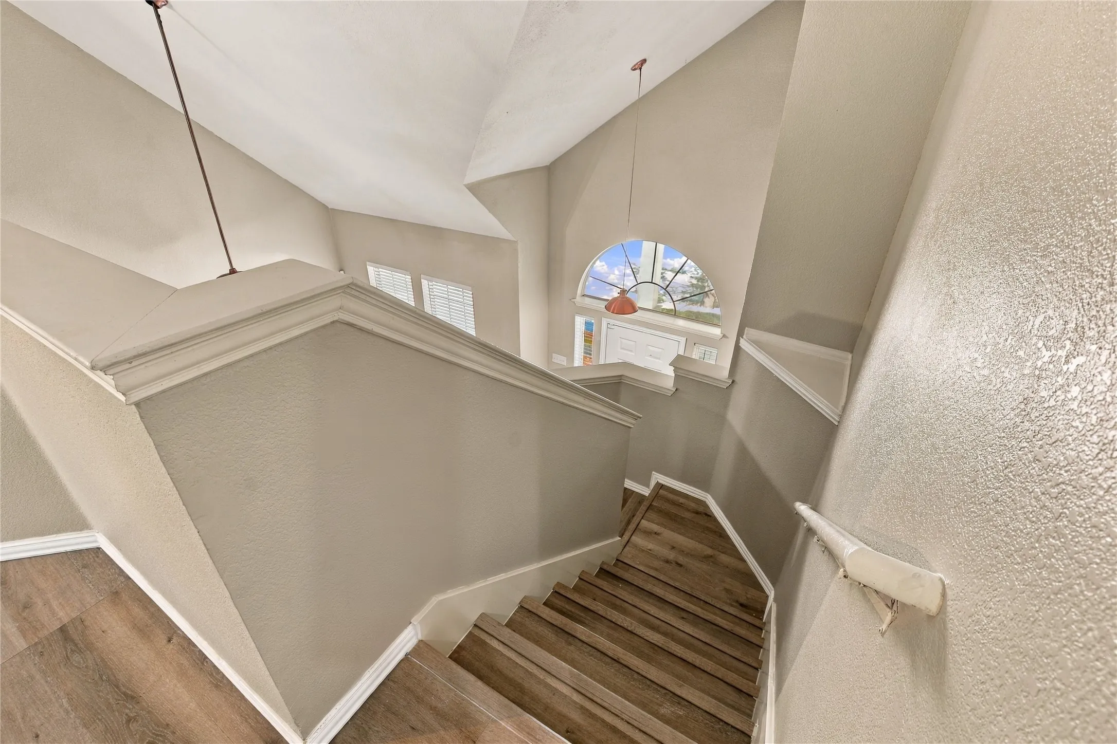 Vaulted ceiling, arched transom window, wood-finish flooring, white trim, and a white handrail
