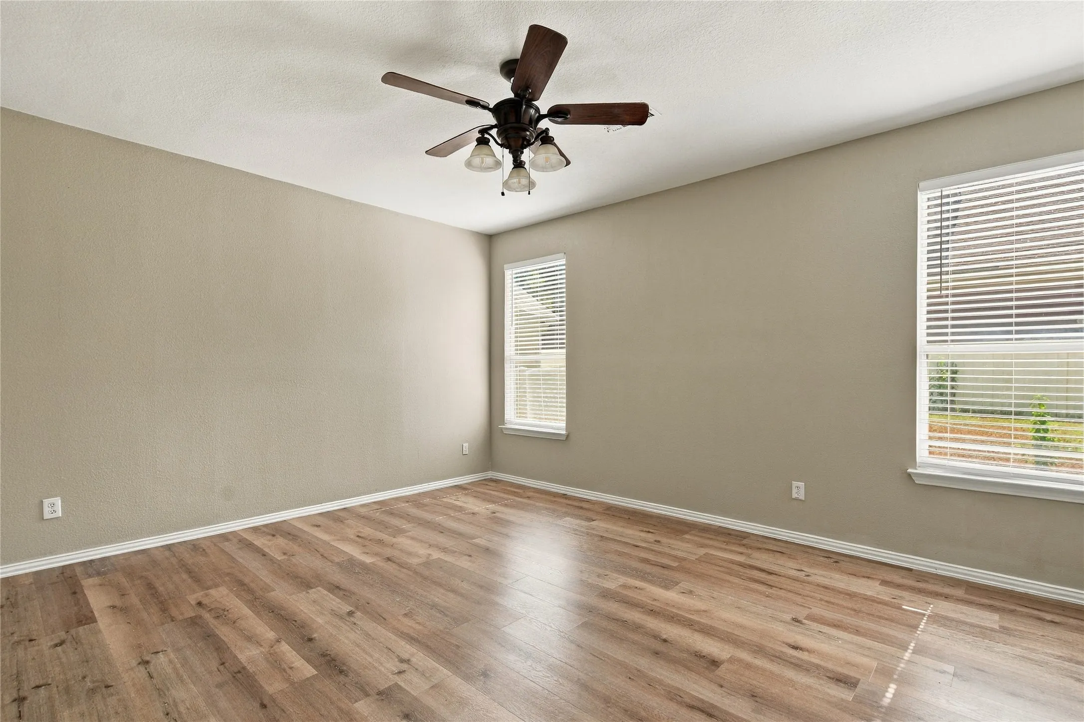 Wood-finish flooring, neutral wall tones, two windows with blinds, and a ceiling fan with integrated lighting
