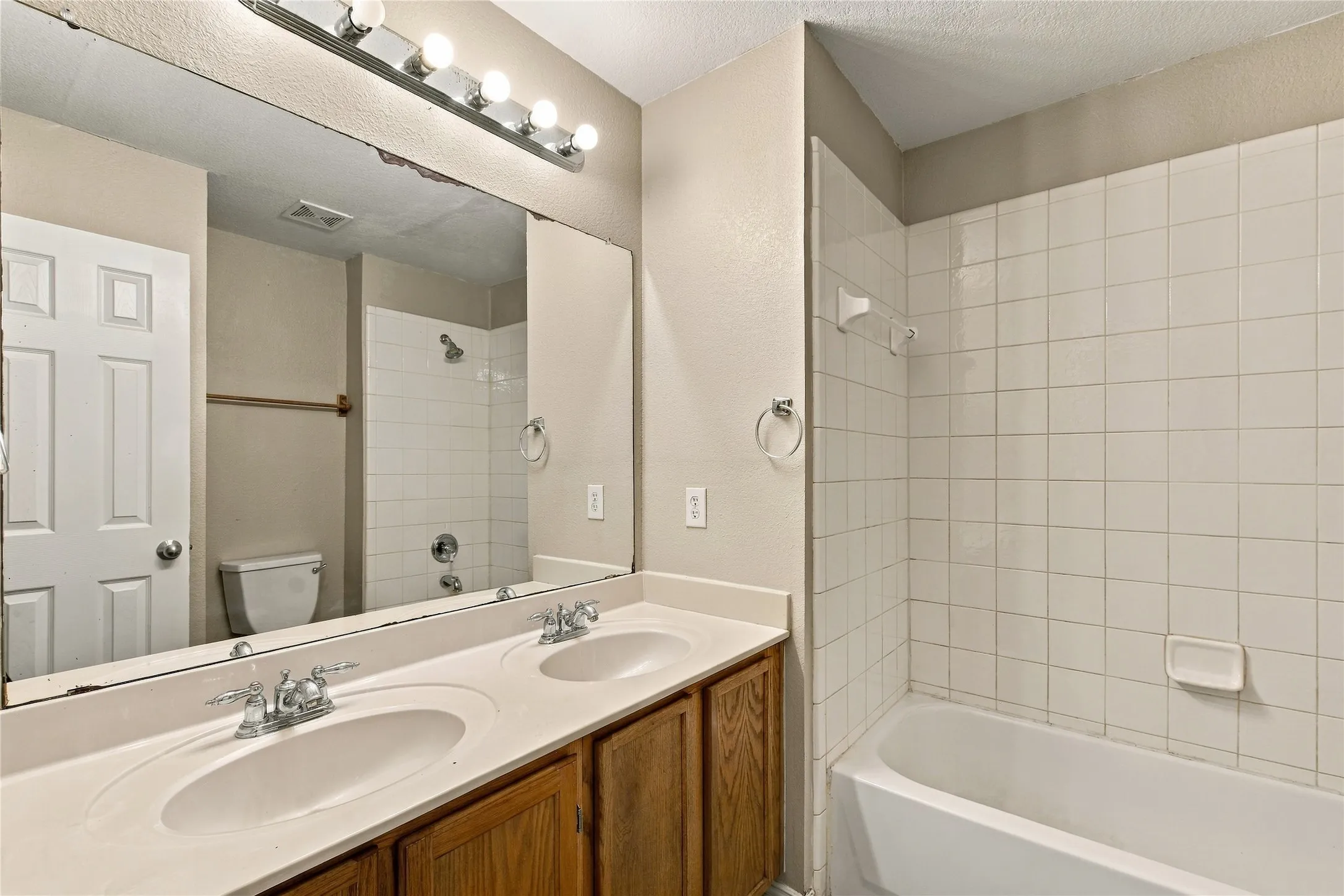 Double vanity with integrated sinks, wood-finish cabinetry, and a full-width mirror