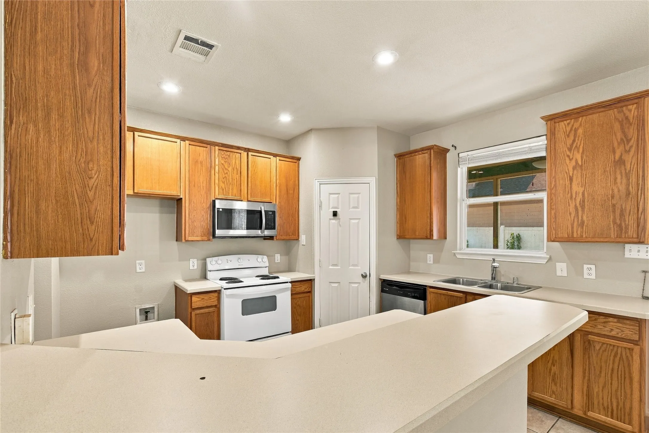 Kitchen featuring wood-finish cabinetry, light-toned countertops, and a double-basin sink with stainless steel faucet