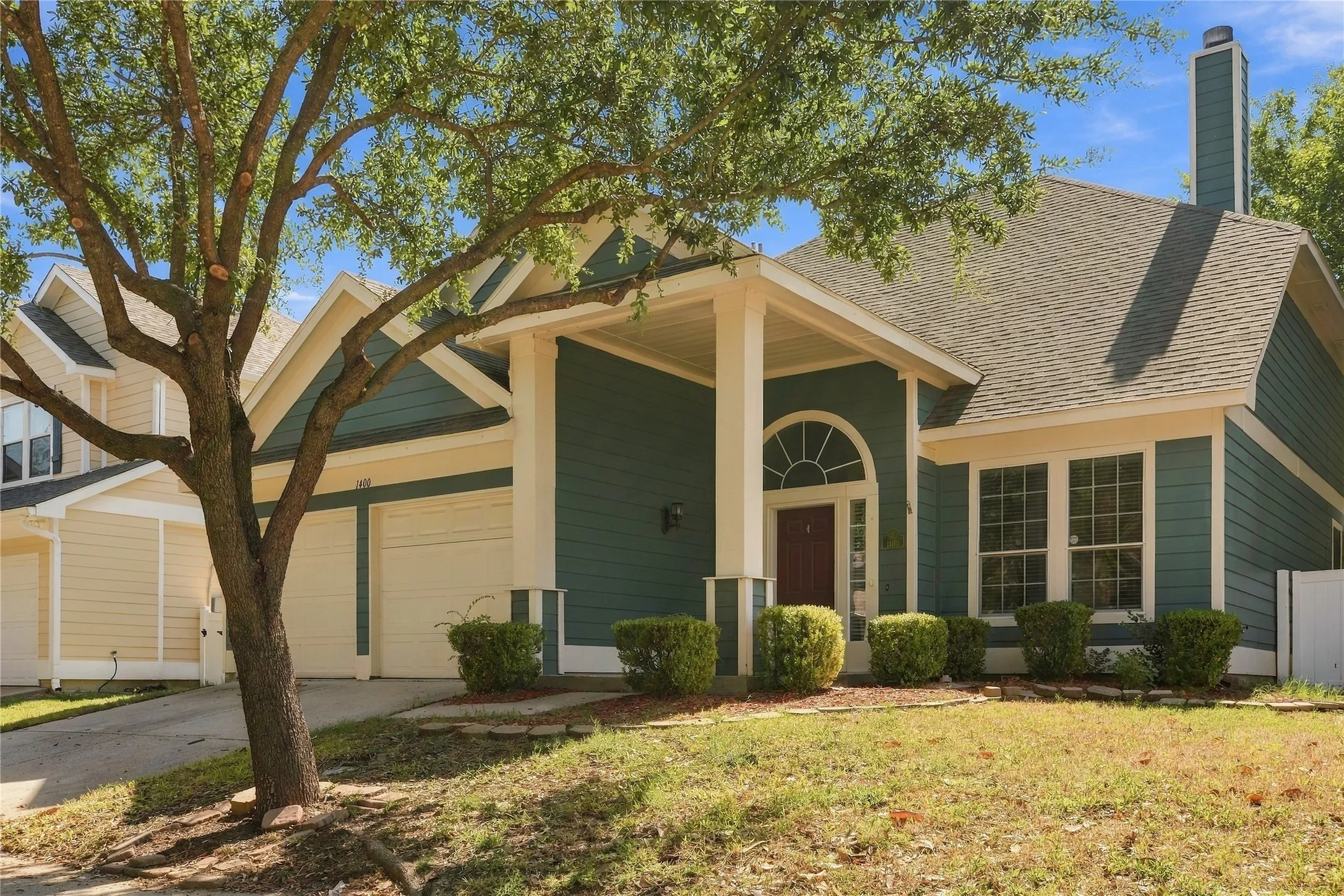 Inviting front exterior featuring a covered entry, arched transom window, two-car garage, and established landscaping