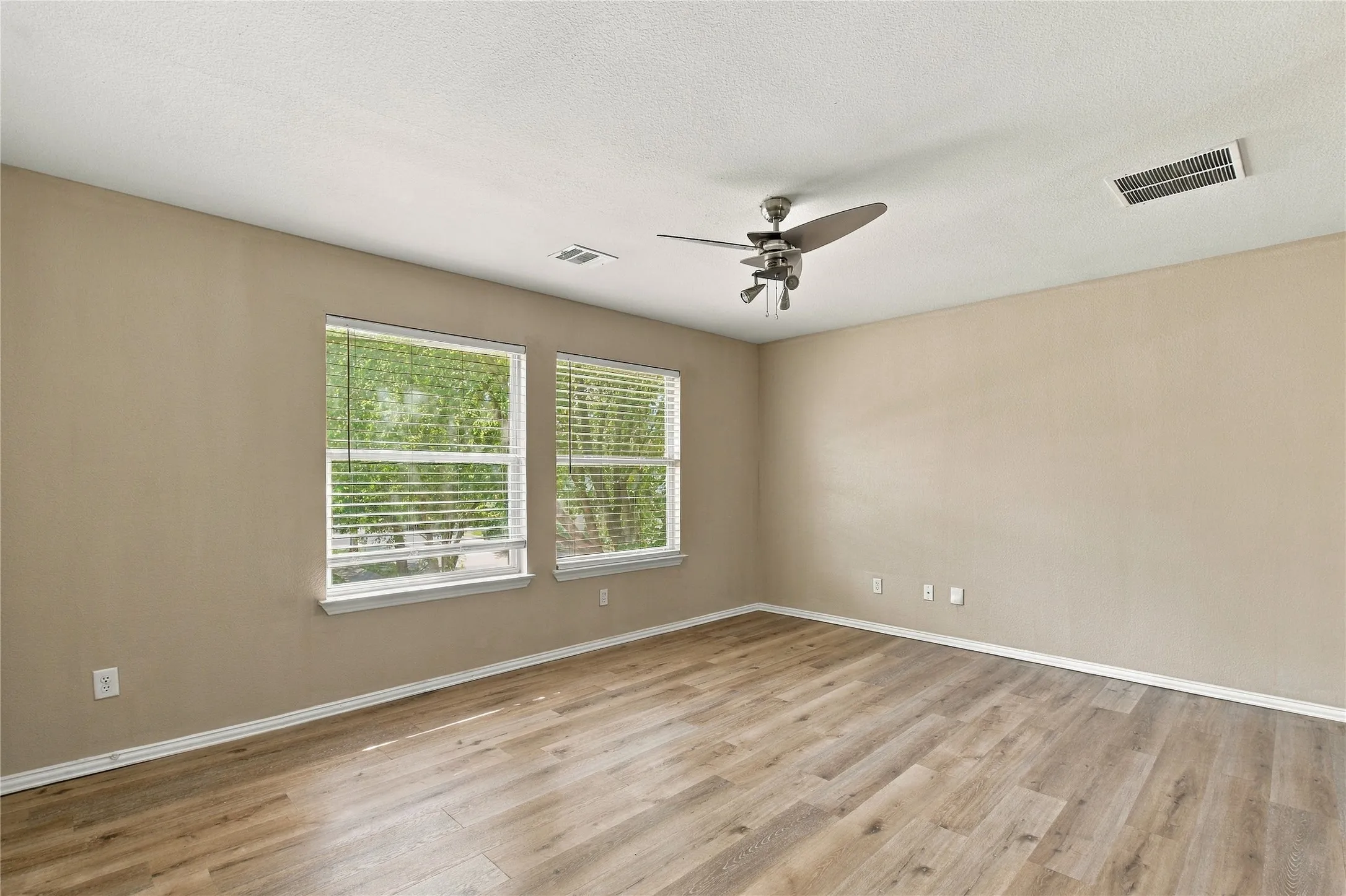 Dual windows with blinds, wood-finish flooring, and a ceiling fan