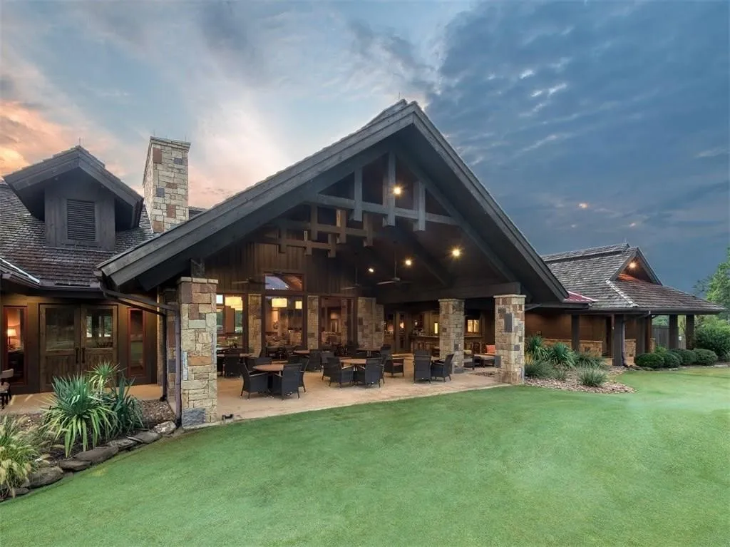 Back of house featuring stone siding, a patio area, a yard, and a chimney