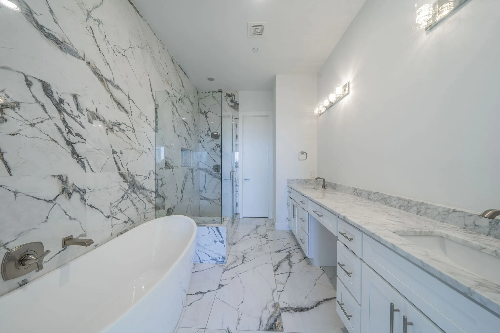 Bathroom with double vanity, a freestanding bath, a marble finish shower, light marble finish floors, and stone wall