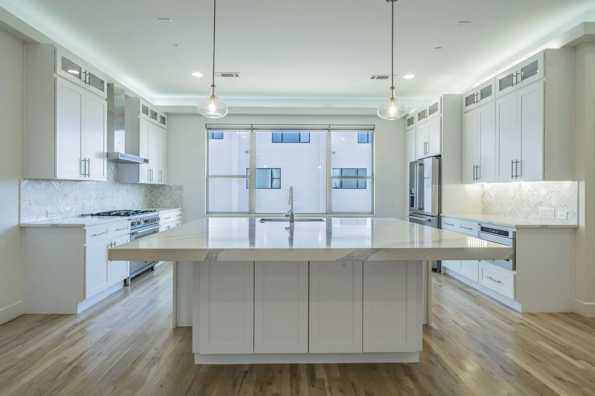 Kitchen featuring decorative backsplash, glass insert cabinets, wall chimney exhaust hood, white cabinets, and recessed lighting