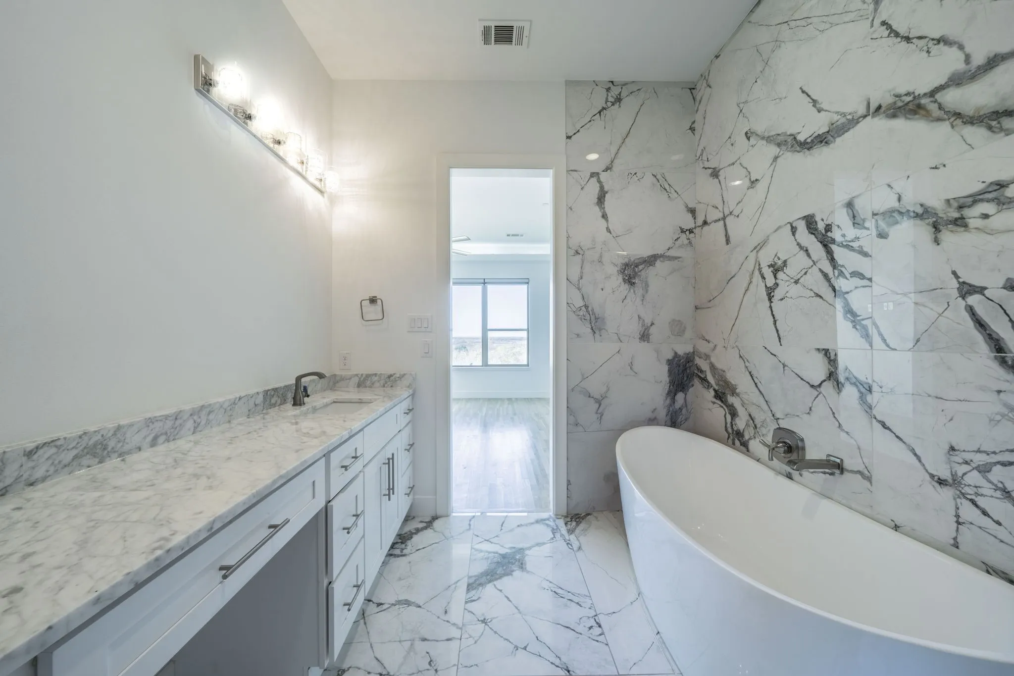 Bathroom featuring vanity, a freestanding tub, light marble finish floors, and stone wall