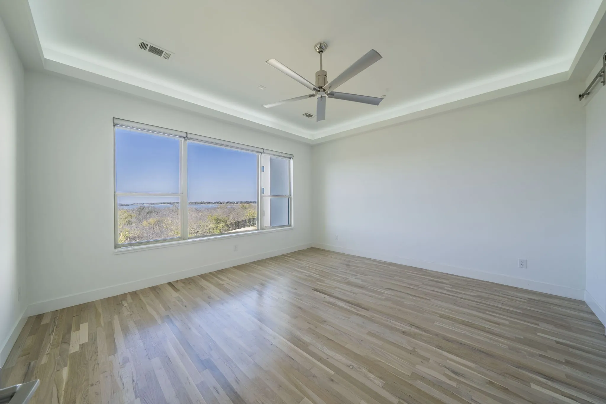 Featuring a raised ceiling, light wood finished floors, and a ceiling fan