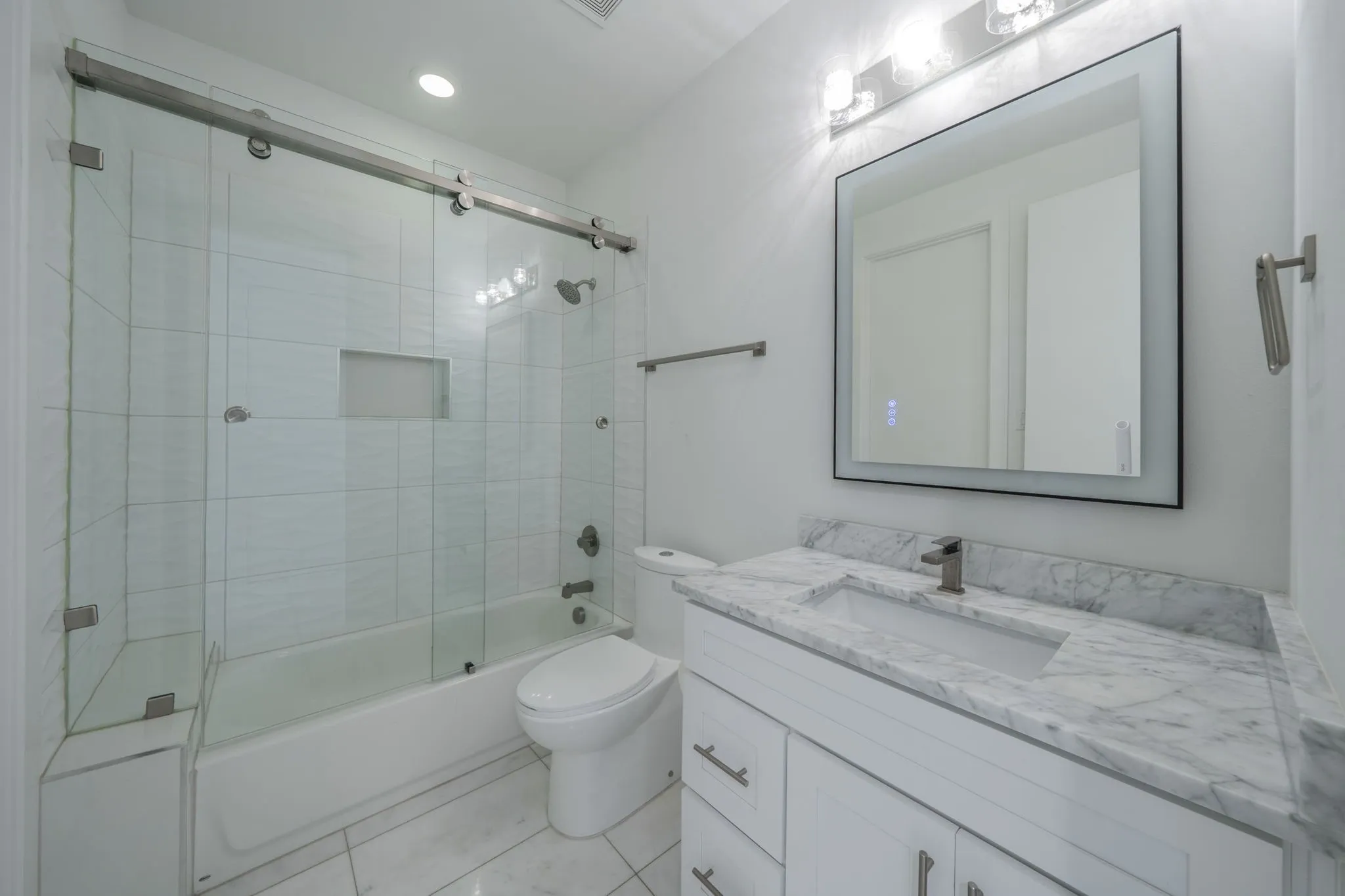 Bathroom with bath / shower combo with glass door, vanity, recessed lighting, and light tile patterned floors. 1st level bath