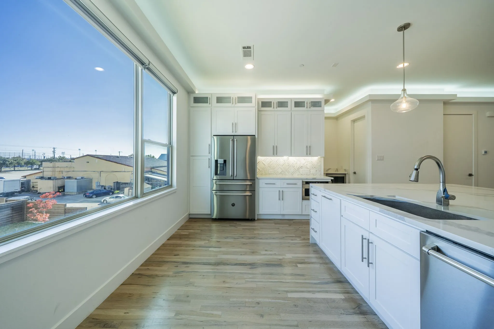 Kitchen with white cabinetry, appliances with stainless steel finishes, decorative backsplash, pendant lighting, and light stone countertops