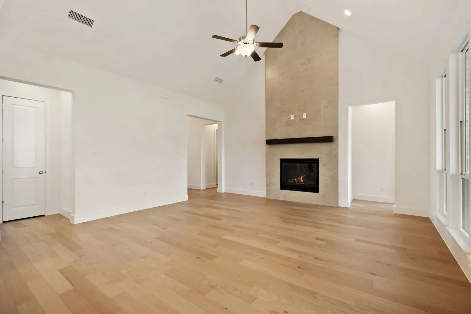 Unfurnished living room with a ceiling fan, lofted ceiling, light wood-style floors, and a tiled fireplace