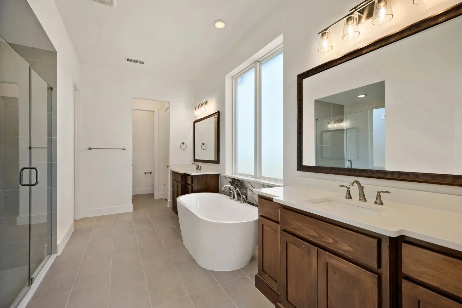 Bathroom with two vanities, a freestanding bath, a shower stall, light tile patterned floors, and recessed lighting