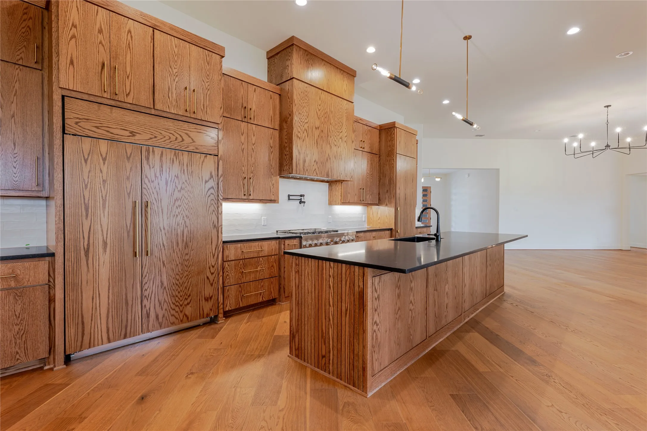Kitchen featuring paneled built in refrigerator, an island with sink, pendant lighting, light wood finished floors, and decorative backsplash