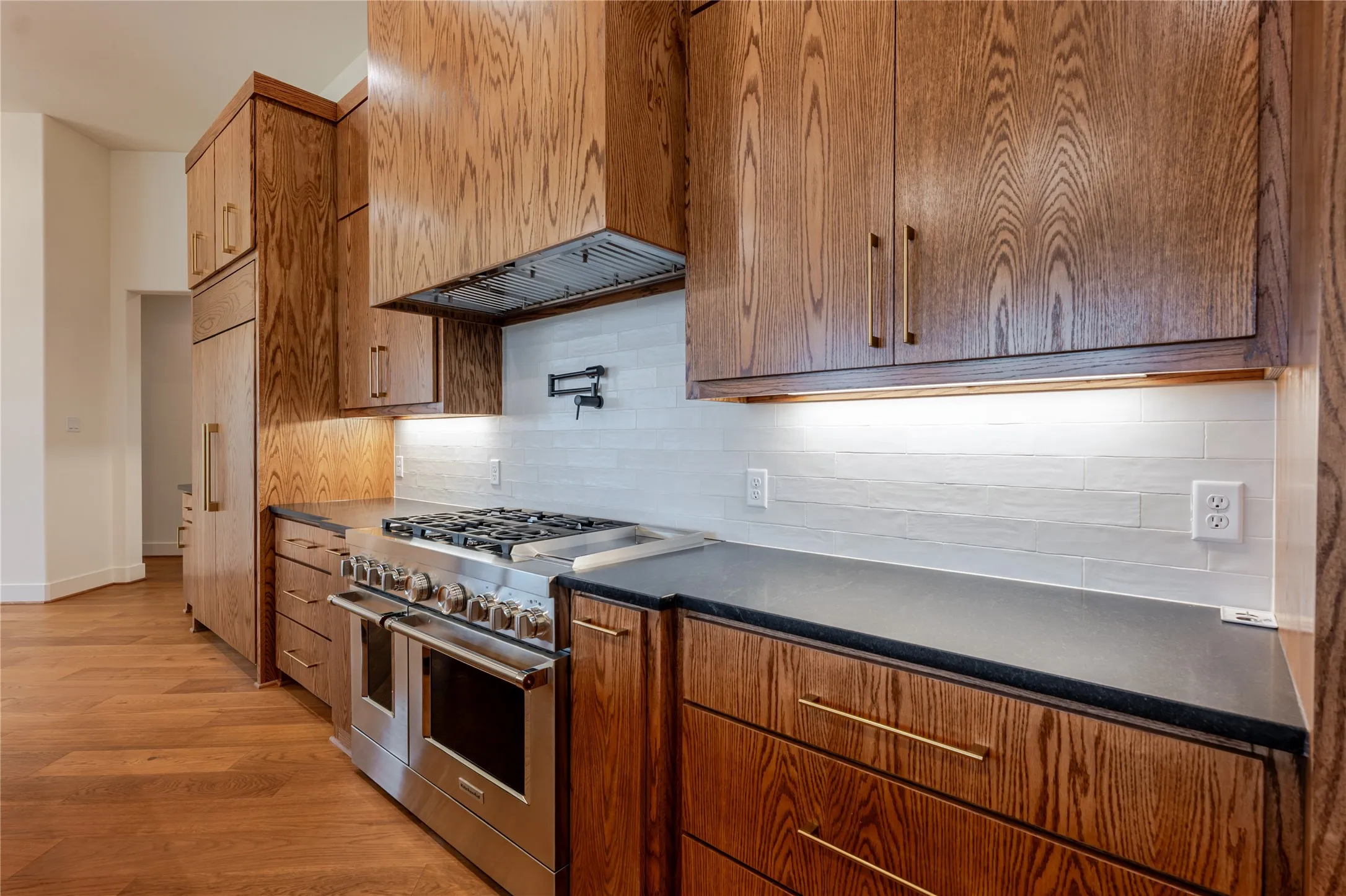Kitchen featuring premium appliances, range hood, light wood-style floors, and brown cabinetry