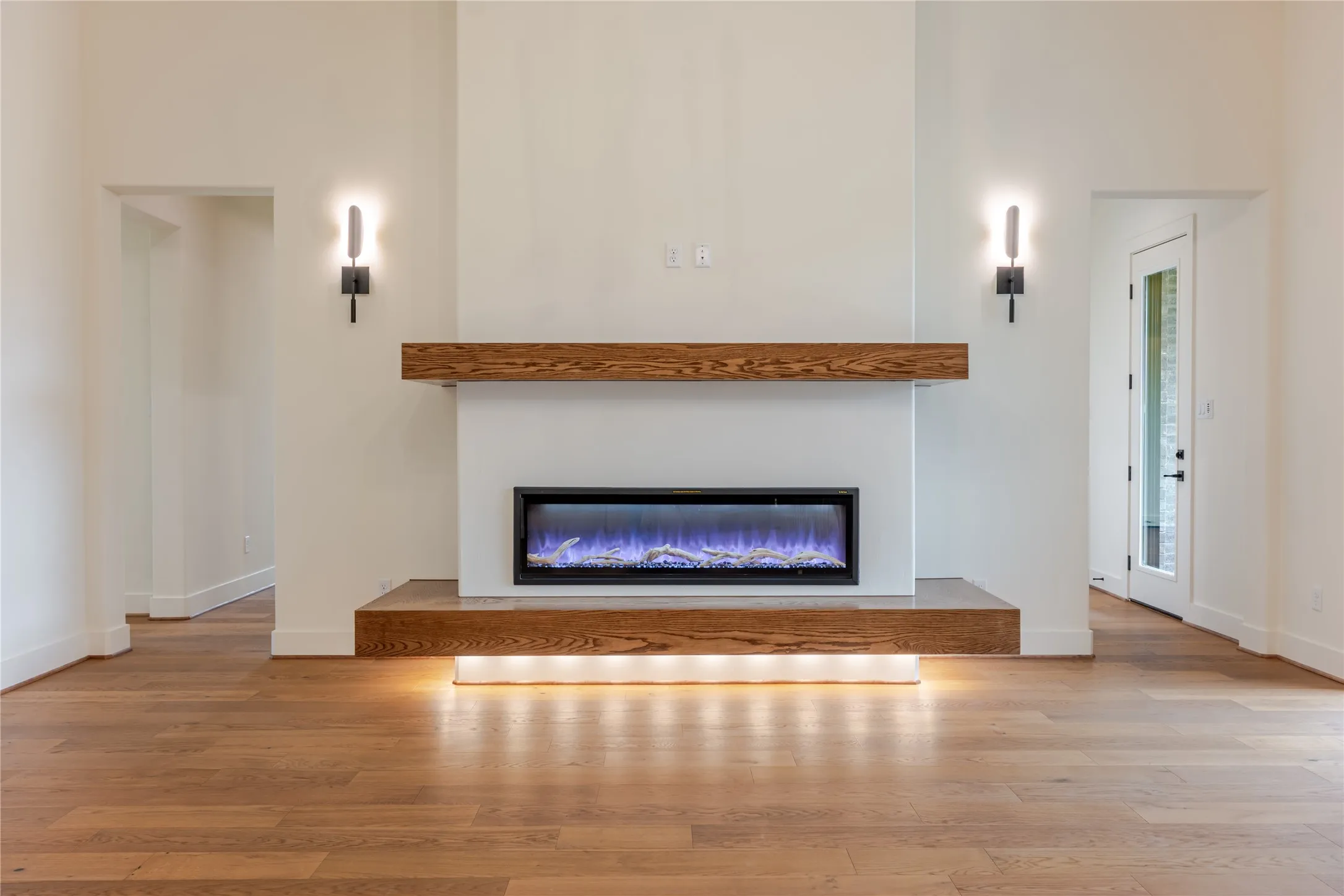 Living room with a glass covered fireplace, light wood finished floors, and a towering ceiling