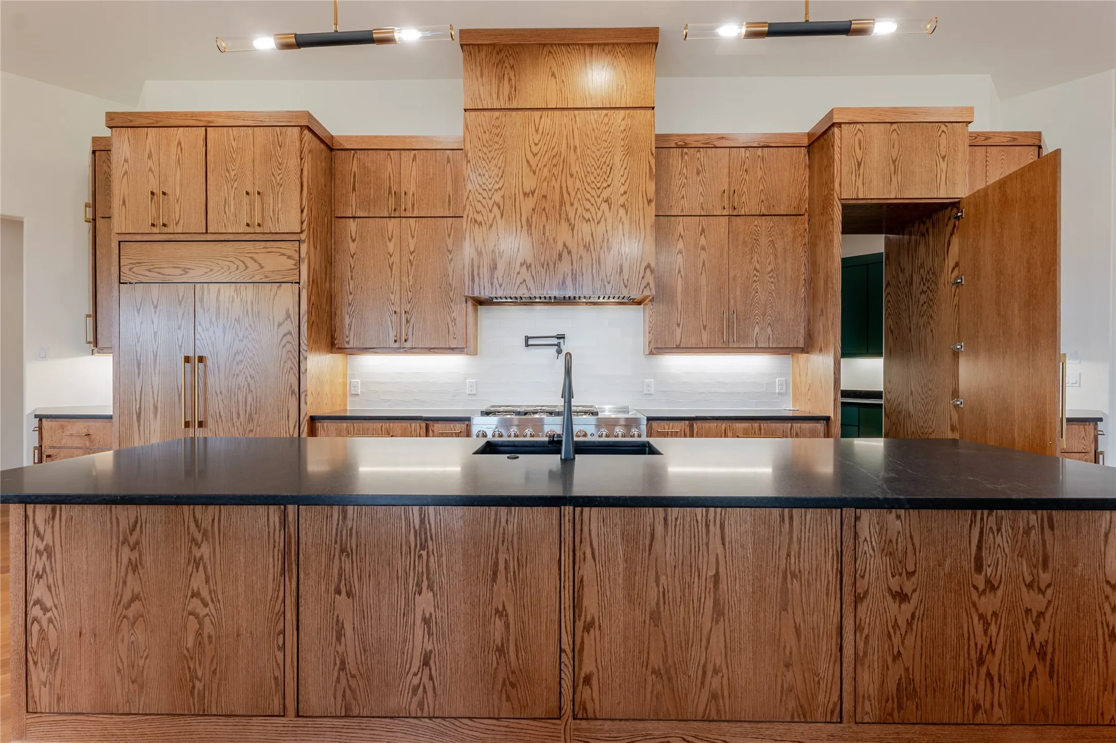 Kitchen featuring decorative backsplash, a spacious island, stainless steel gas cooktop, and dark stone countertops
