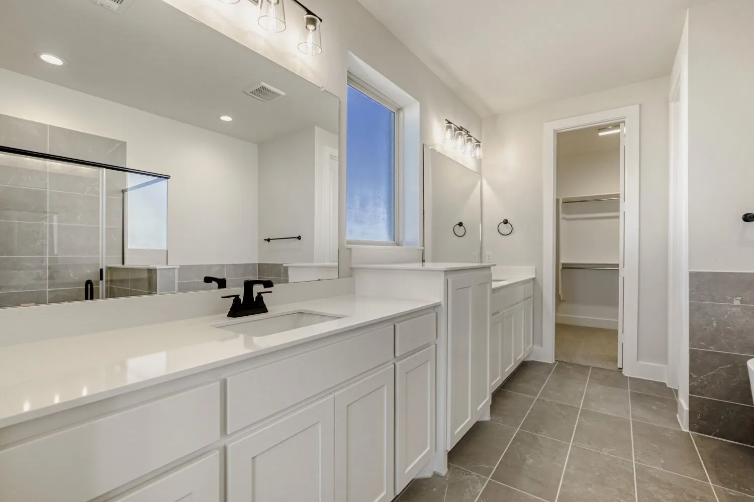 Full bathroom featuring two vanities, a shower stall, dark tile patterned floors, and a spacious closet