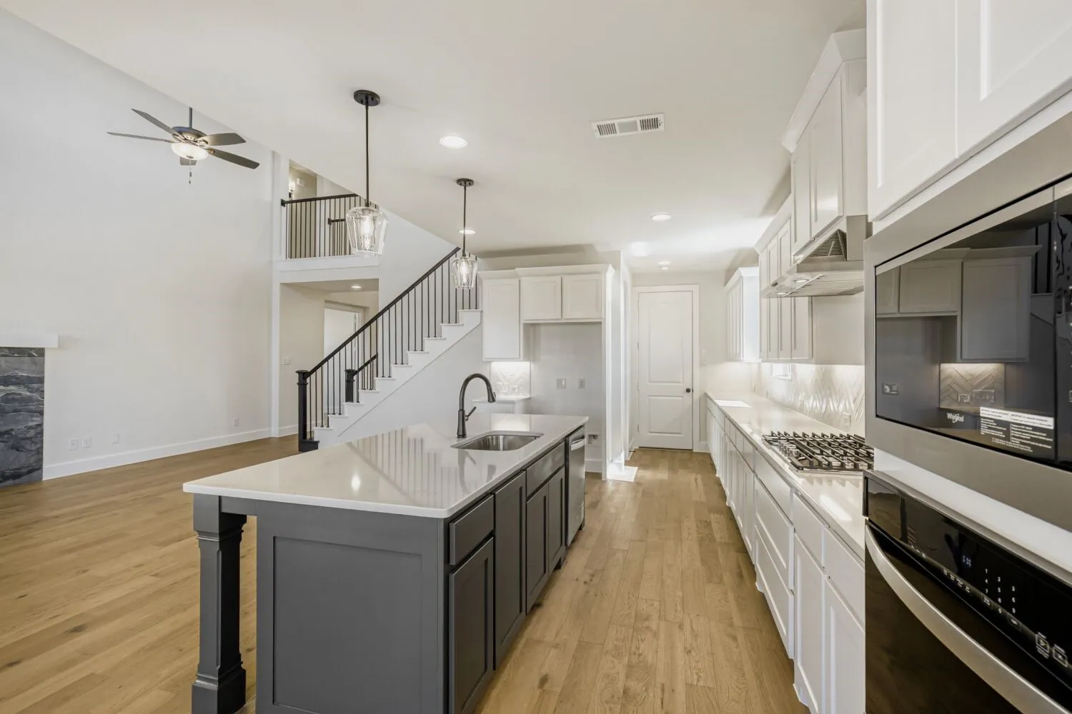 Two tone kitchen featuring dual tone cabinets, stainless steel appliances, a kitchen island with sink, light wood-style floors, and a kitchen breakfast bar