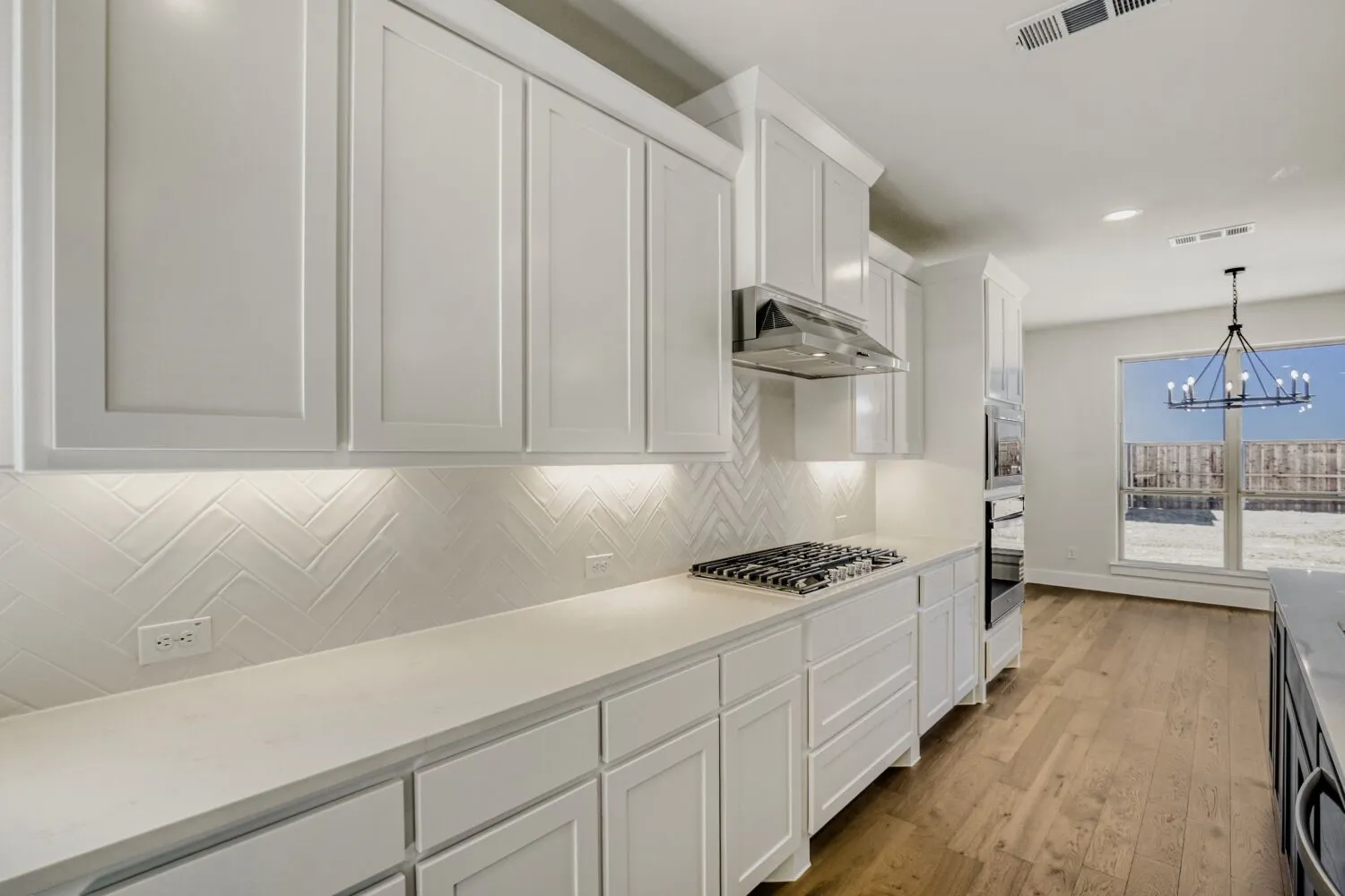 Kitchen featuring hanging lights, white cabinetry, light wood finished floors, light stone counters, and ventilation hood