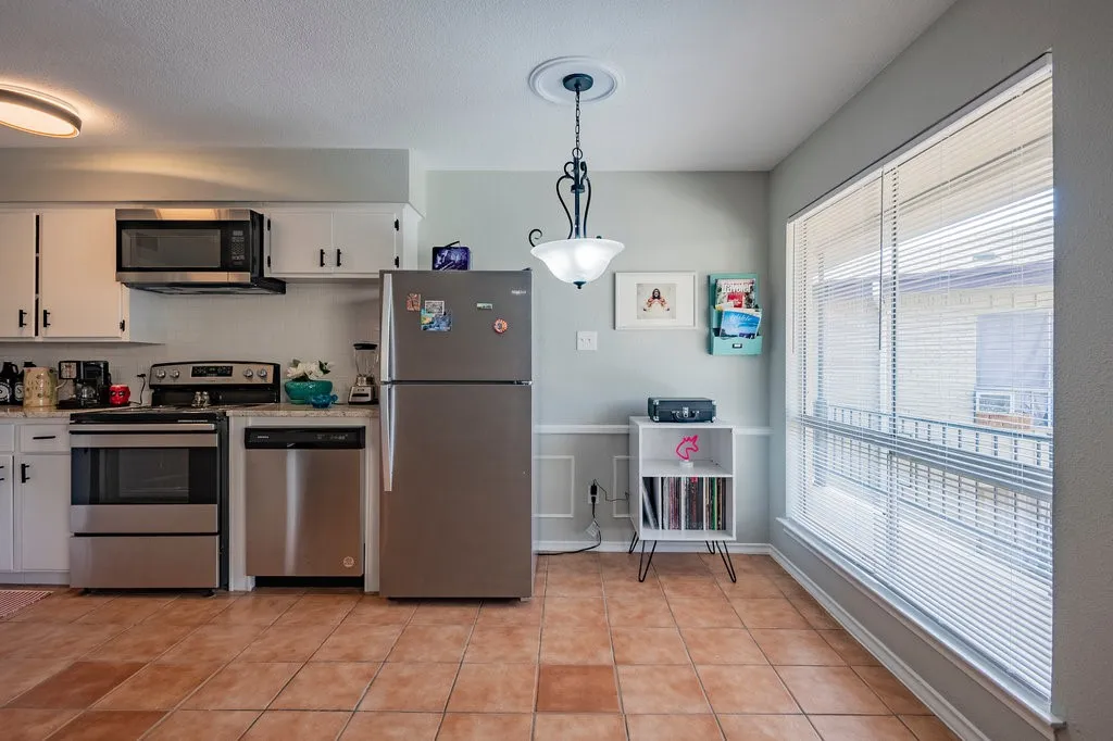 Kitchen featuring white cabinetry, stainless steel appliances, decorative light fixtures, light tile patterned flooring, and a wainscoted wall