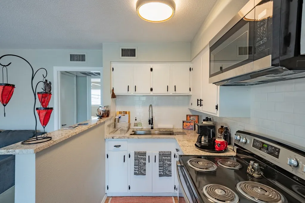 Kitchen featuring stainless steel appliances, white cabinets, decorative backsplash, a textured ceiling, and light stone counters