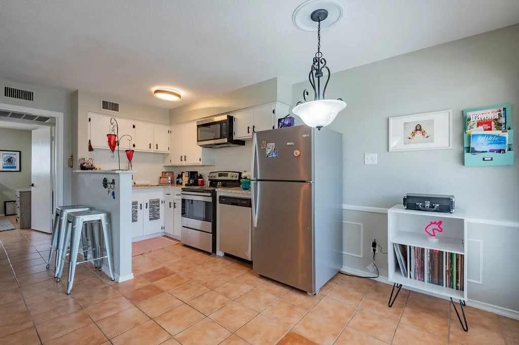 Kitchen with appliances with stainless steel finishes, light countertops, hanging light fixtures, white cabinetry, and light tile patterned floors
