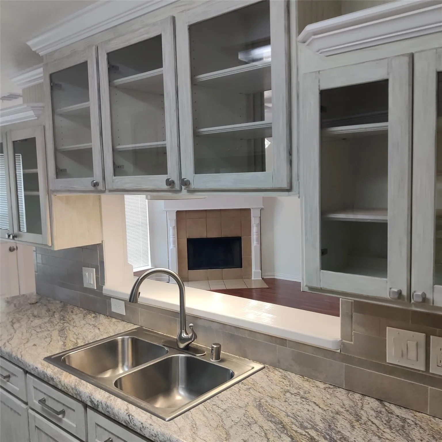 Kitchen with light countertops, glass insert cabinets, and tasteful backsplash