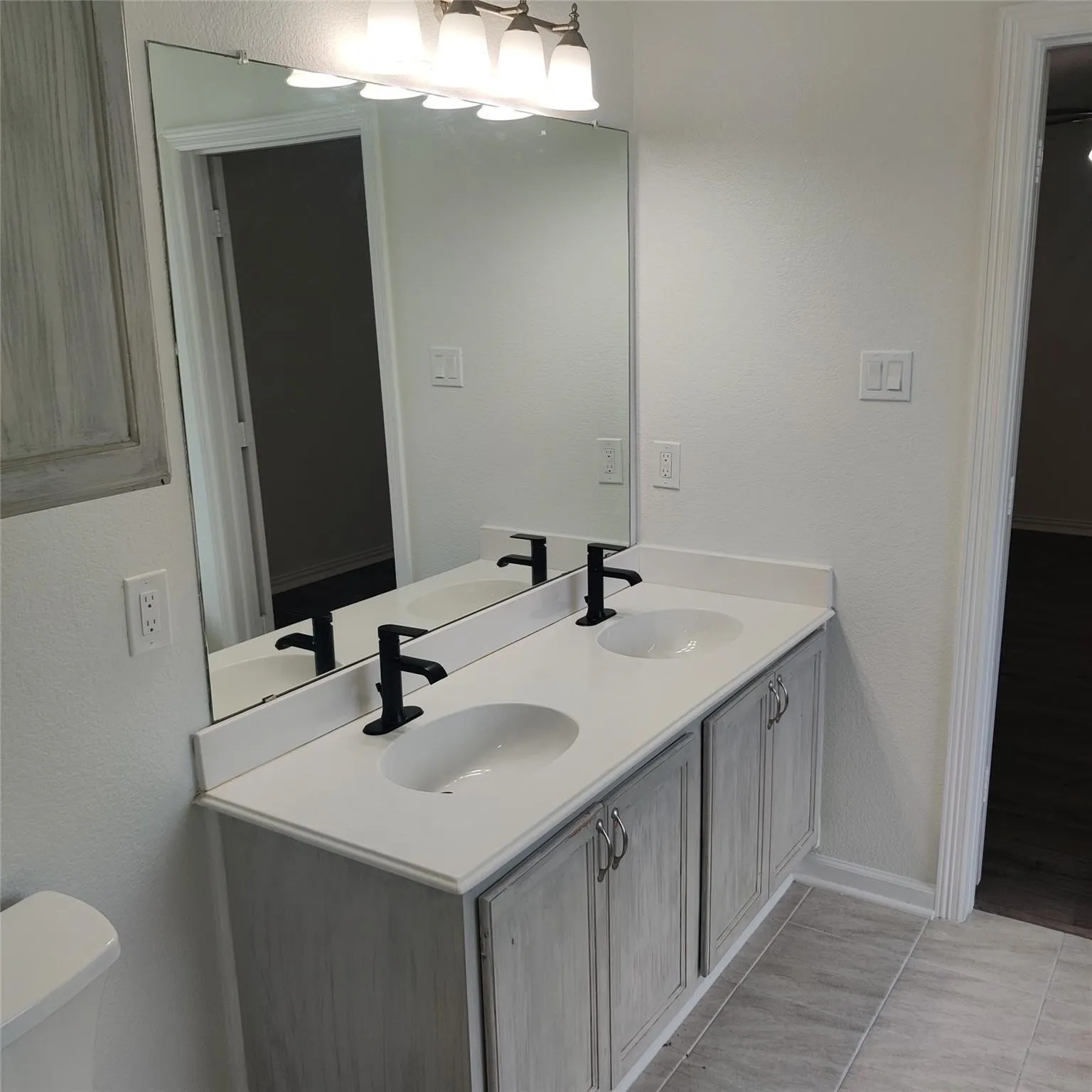 Full bathroom featuring double vanity, a textured wall, and light tile patterned floors