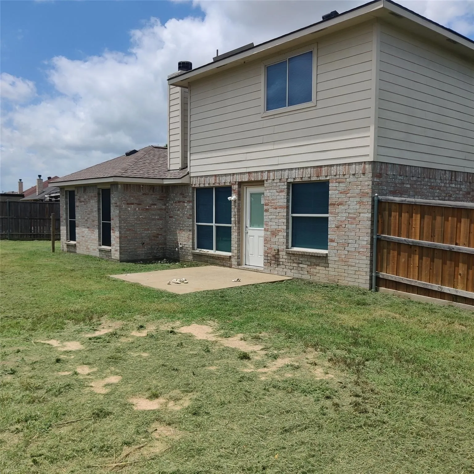 Back of property with a fenced backyard, brick siding, a patio, a chimney, and roof with shingles