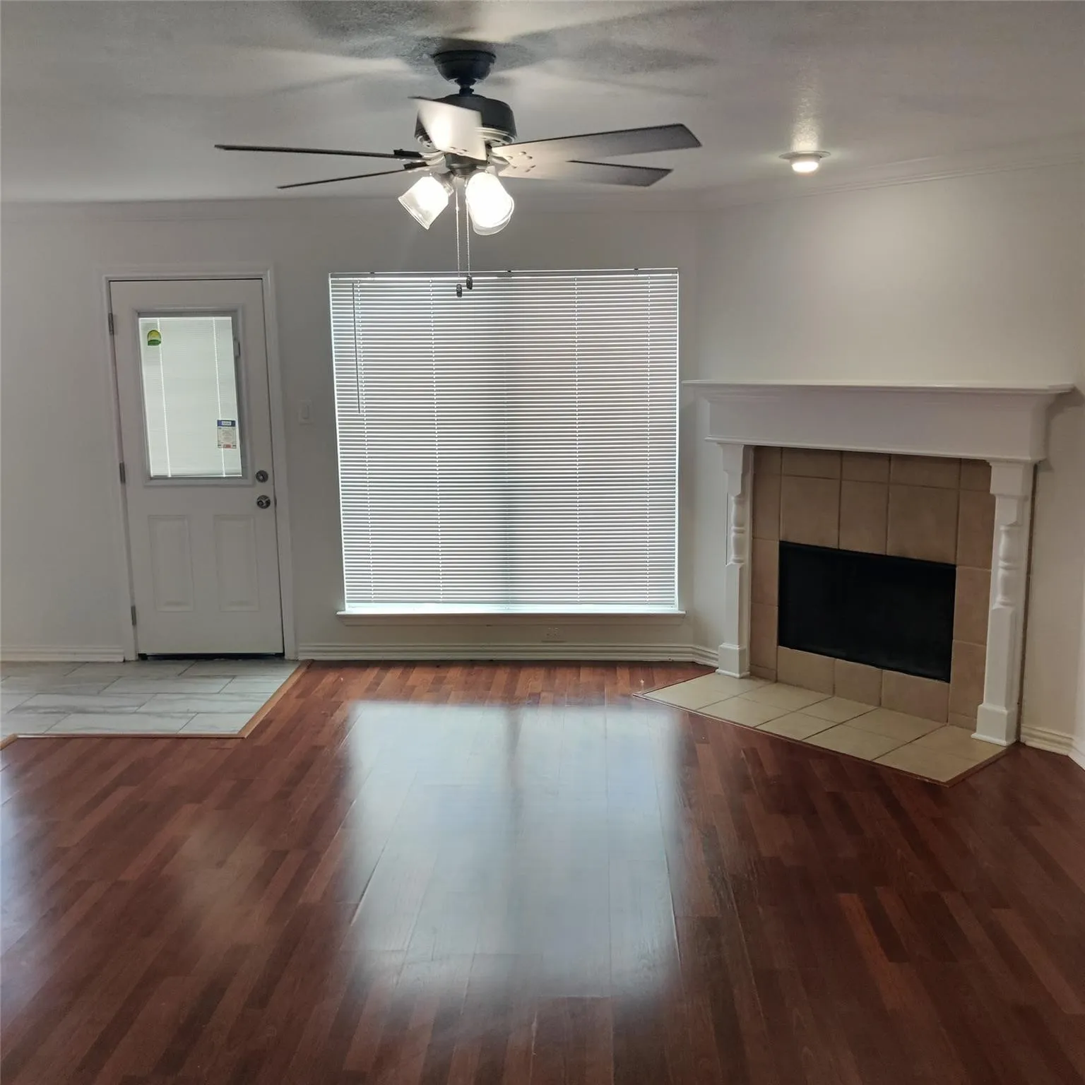 Unfurnished living room with light wood-type flooring, a tile fireplace, ceiling fan, and ornamental molding