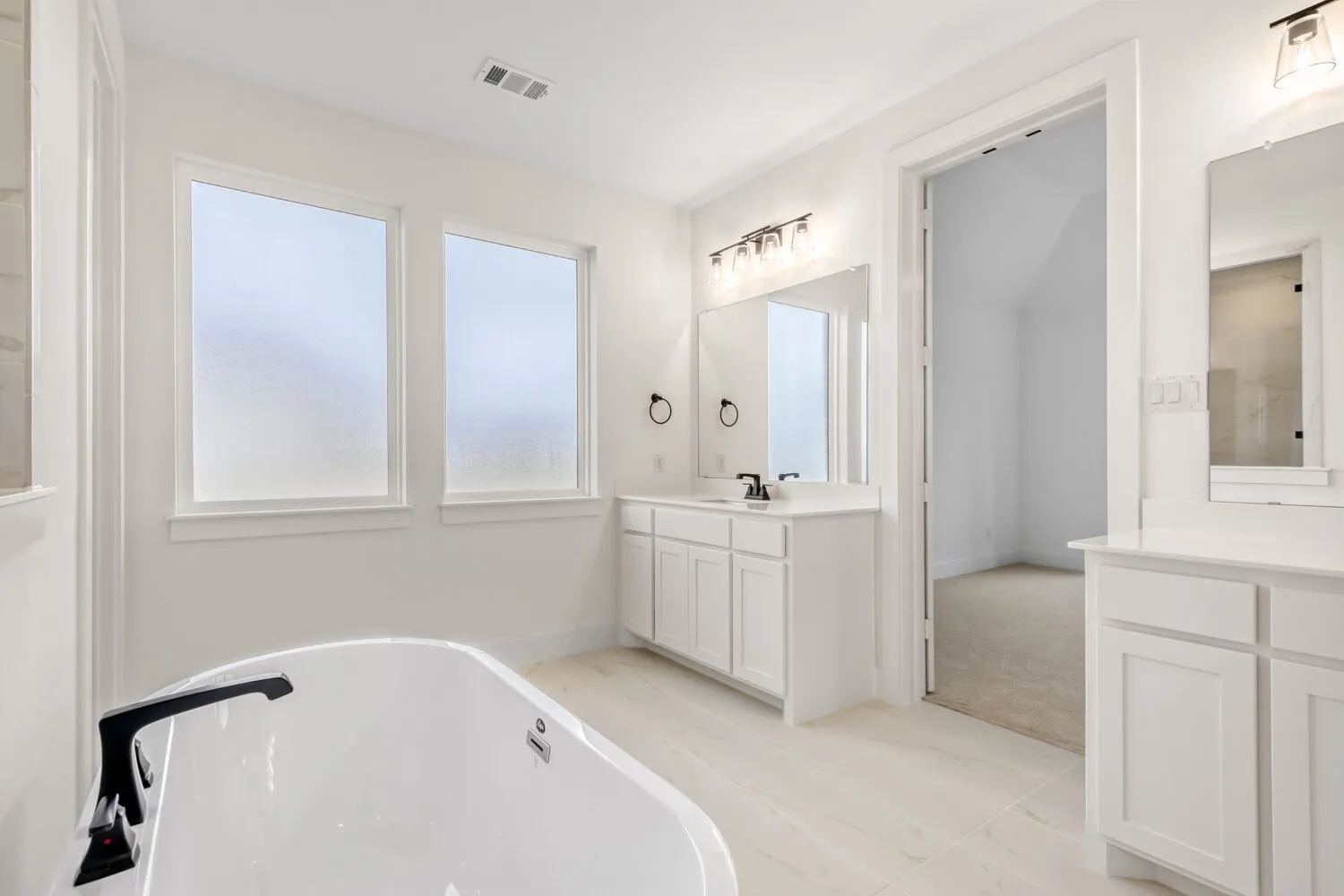 Full bath with a freestanding bath, two vanities, and light tile patterned floors
