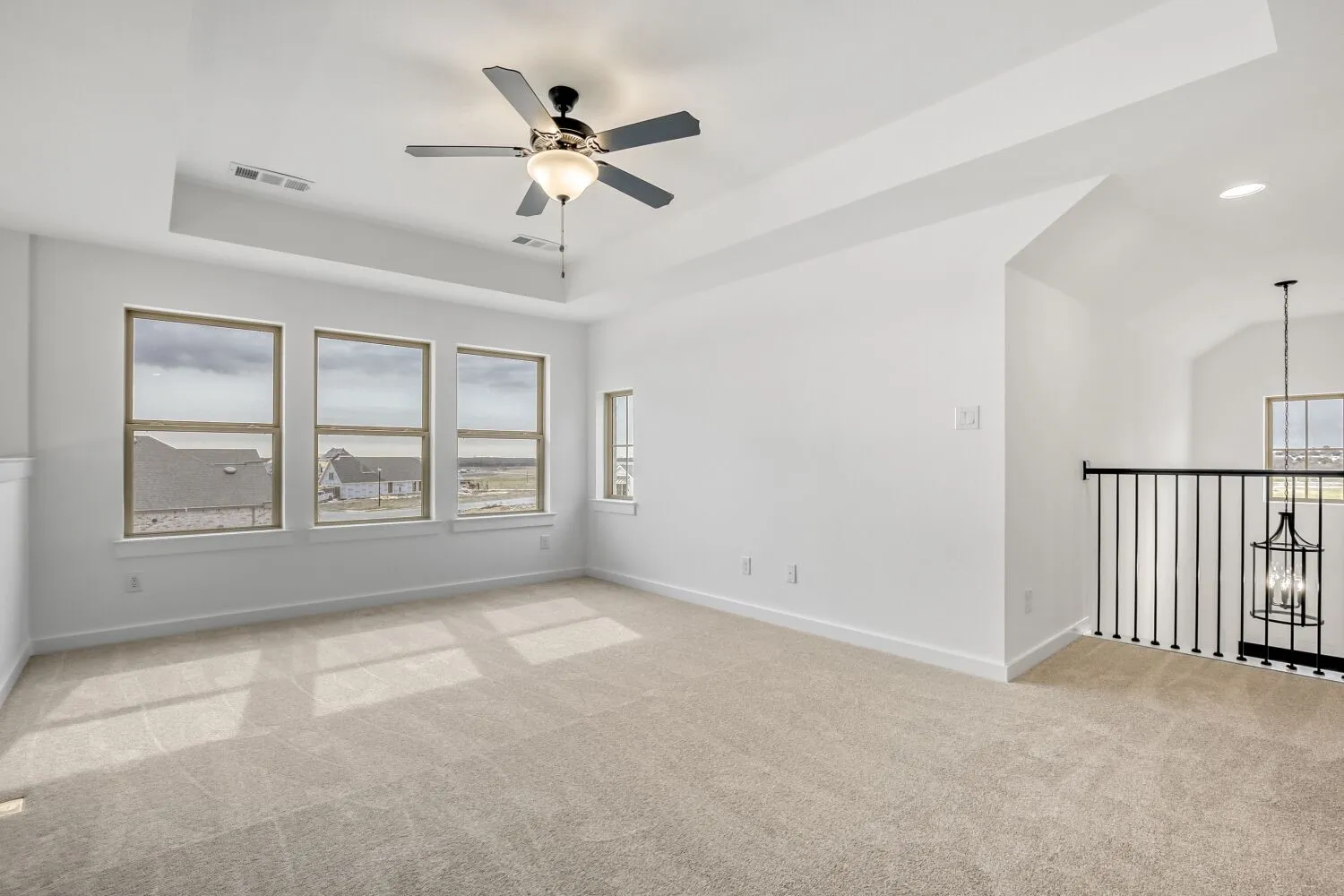 Unfurnished room featuring a tray ceiling, light colored carpet, ceiling fan, and suspended lighting