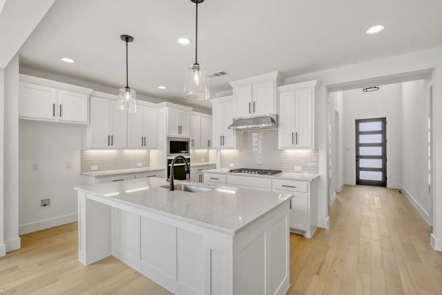 Kitchen featuring white cabinets, light wood-type flooring, light stone countertops, and pendant lighting