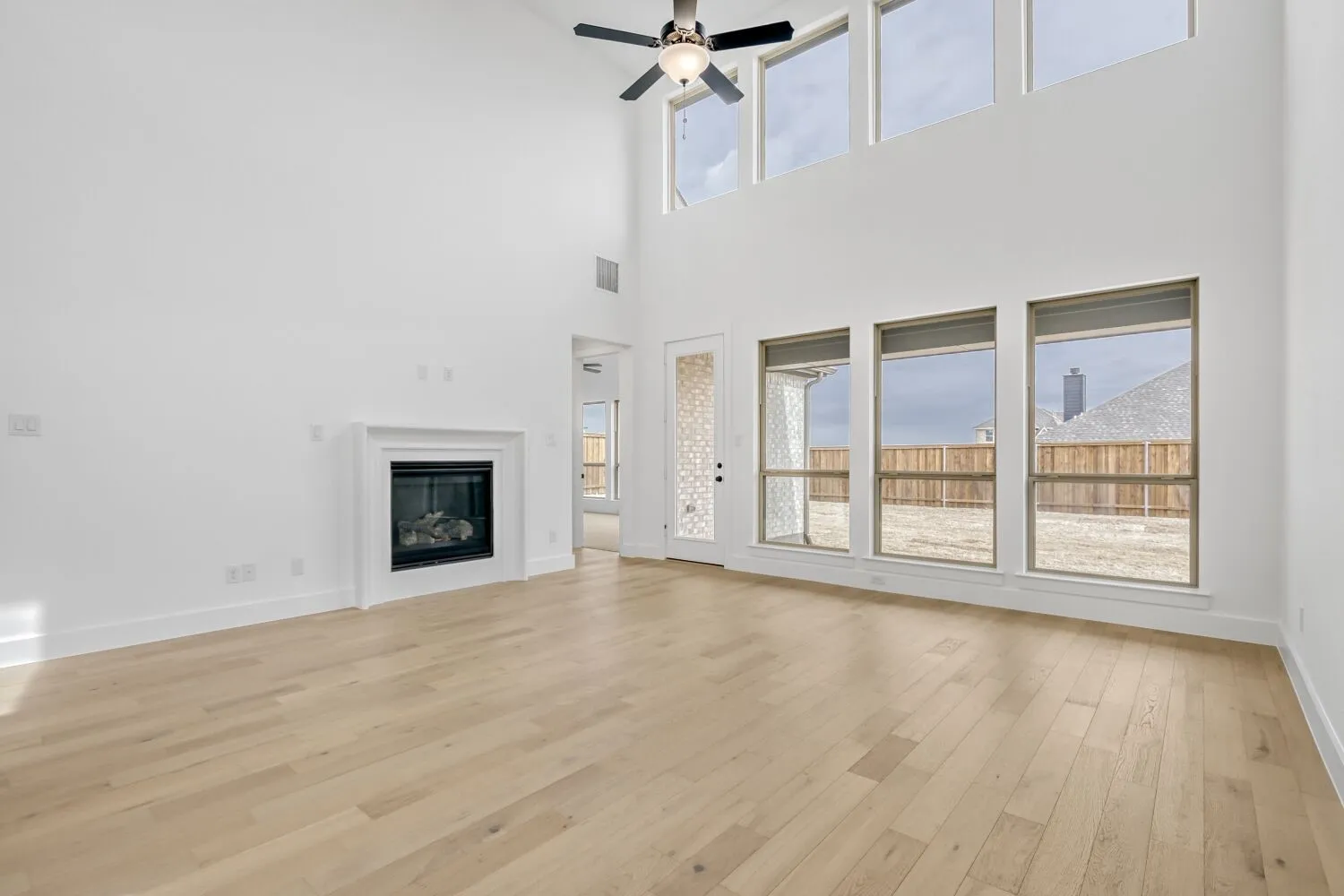 Unfurnished living room with a glass covered fireplace, a ceiling fan, light wood finished floors, and a high ceiling