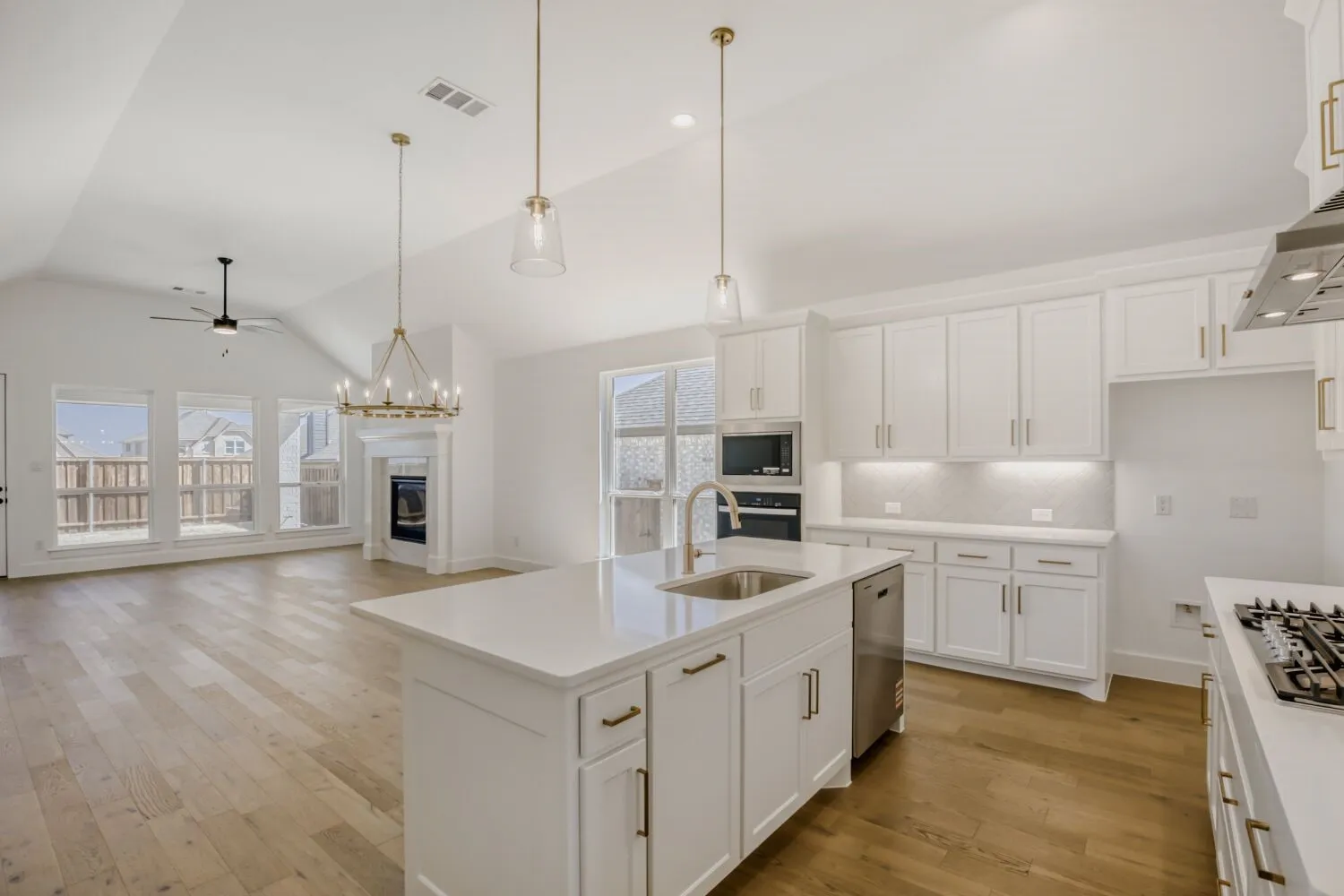 Kitchen featuring white cabinetry, a ceiling fan, a glass covered fireplace, a center island with sink, and a high ceiling