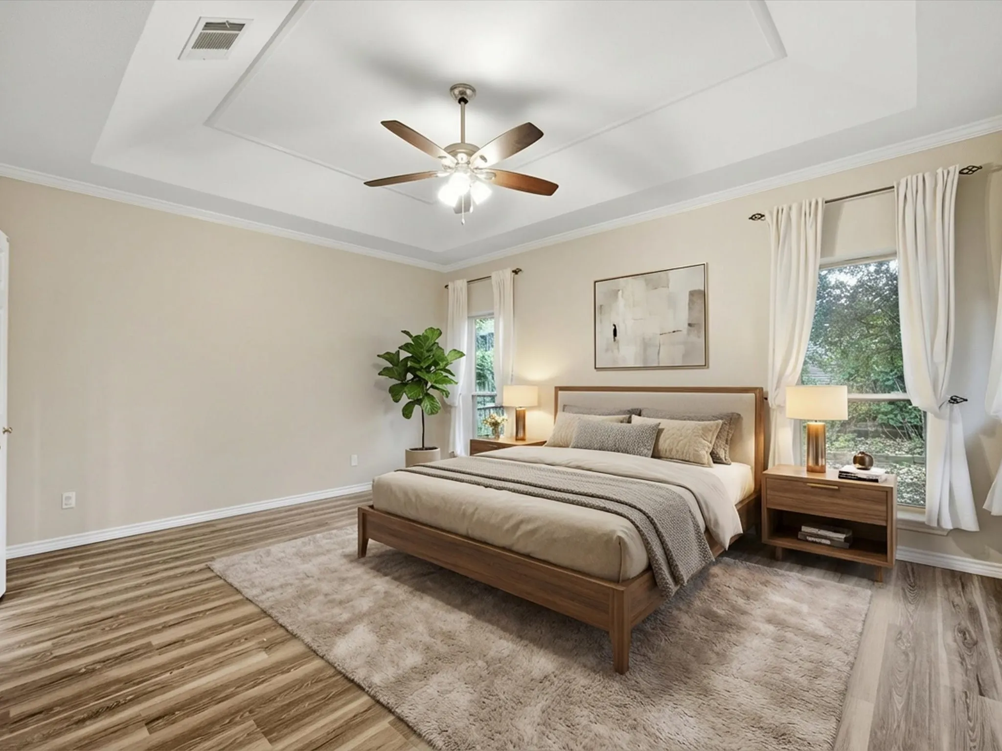 Primary Bedroom featuring a tray ceiling, multiple windows, light wood-type flooring, and crown molding